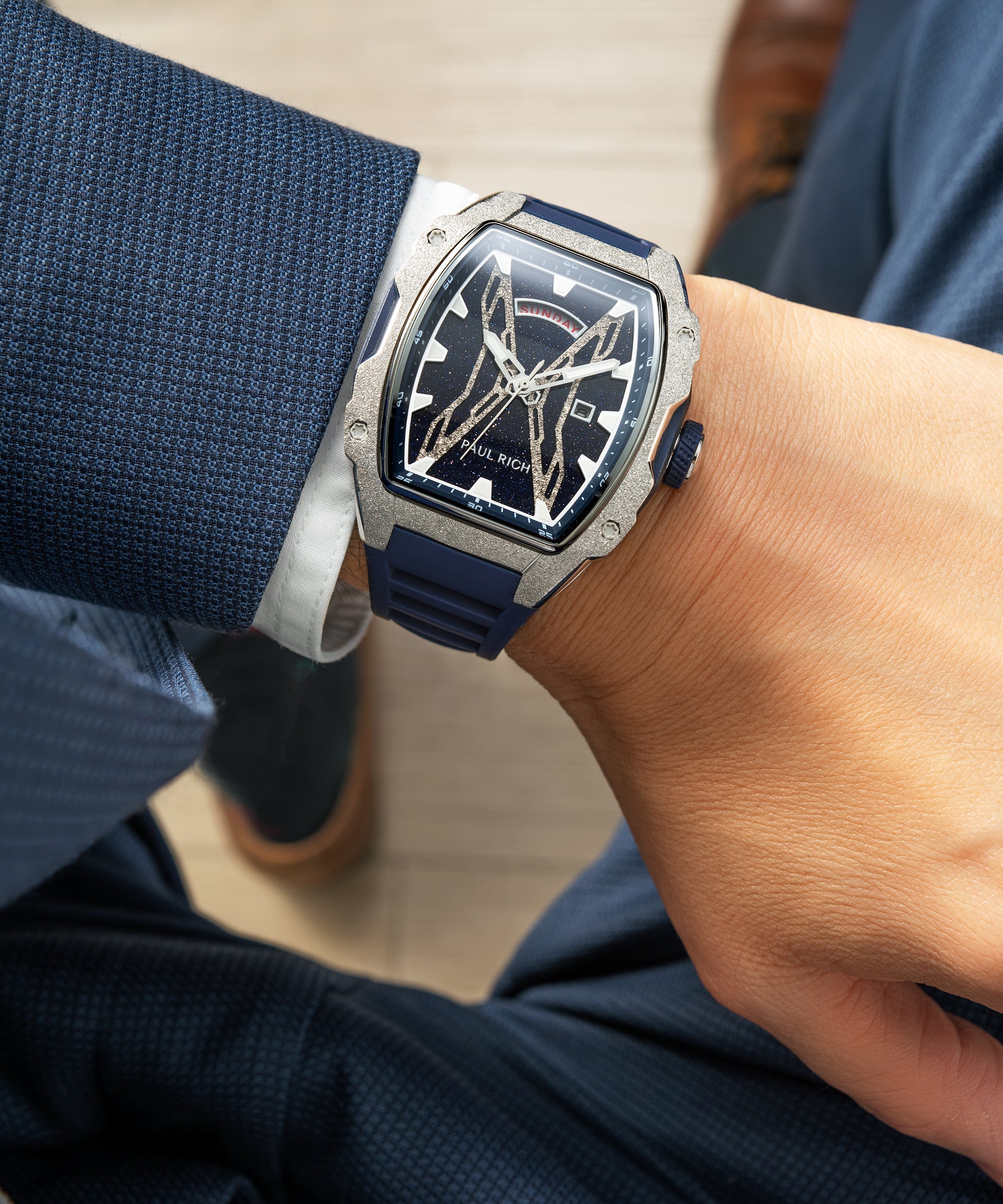 Paul Rich watch with blue aventurine dial, silver frosted bezel, and blue strap worn on wrist with textured navy suit and white cuff.