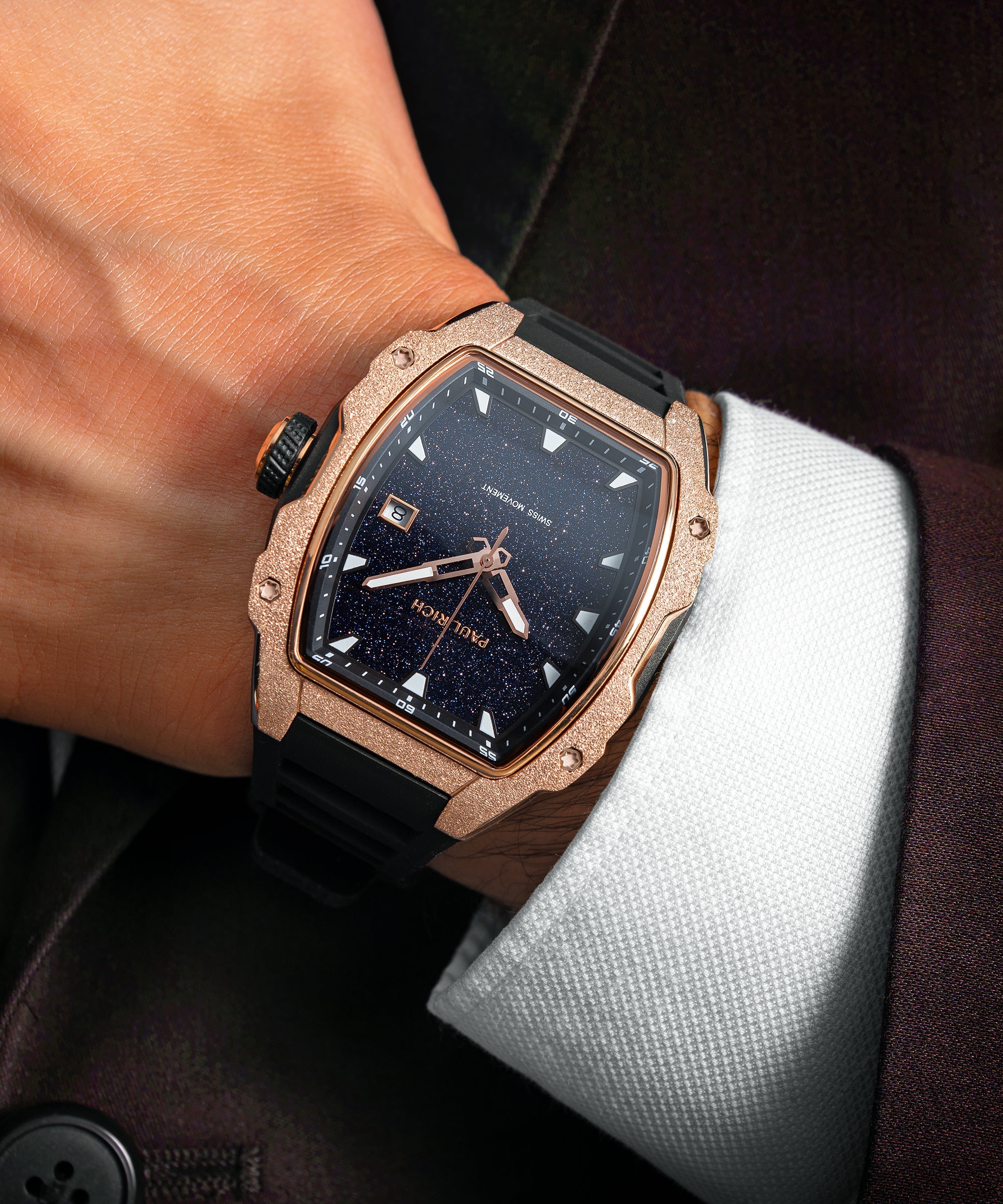 Paul Rich watch with blue aventurine dial and rose gold frosted bezel worn on wrist, paired with white cuff and dark suit jacket.