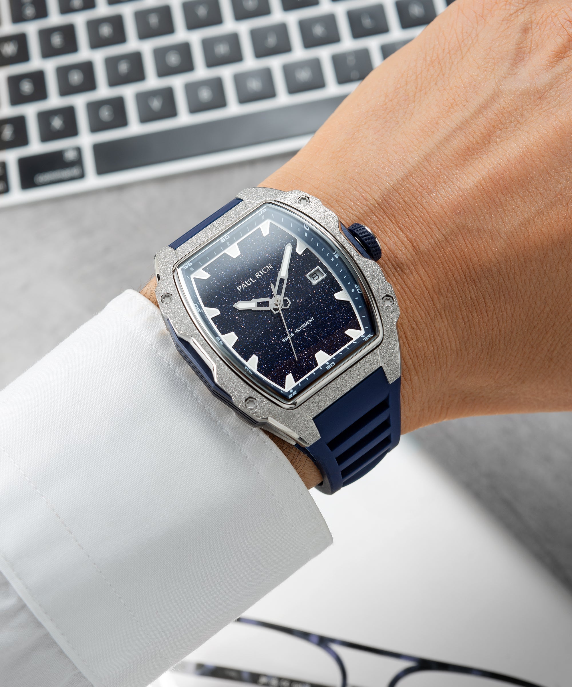 Paul Rich watch with tonneau case, frosted silver bezel, and blue aventurine dial, worn on wrist with white shirt, shown near a keyboard.