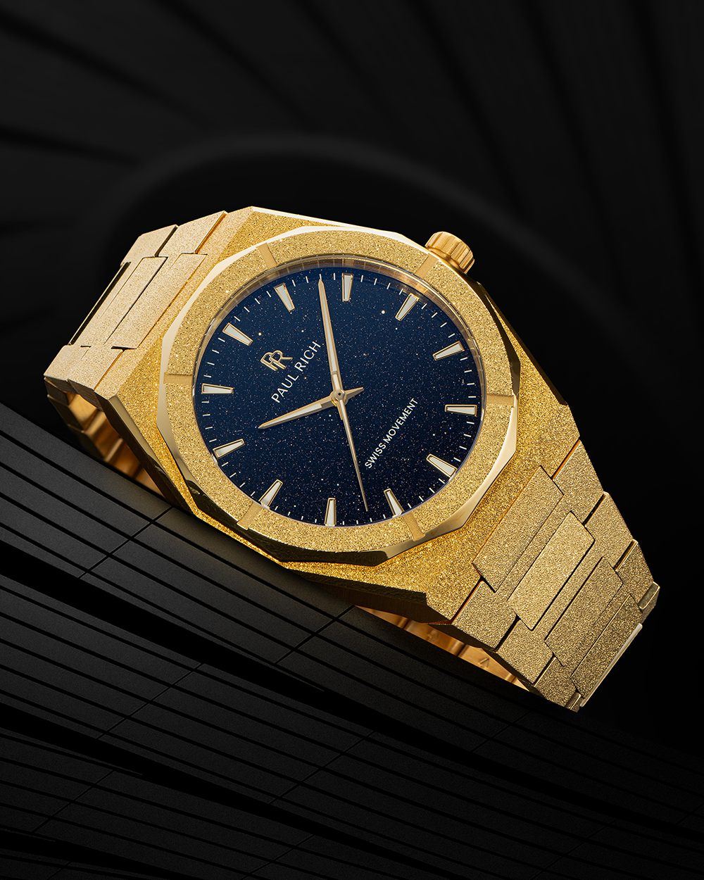 Gold frosted Paul Rich watch with blue aventurine dial and gold markers, resting on a sleek black geometric surface.