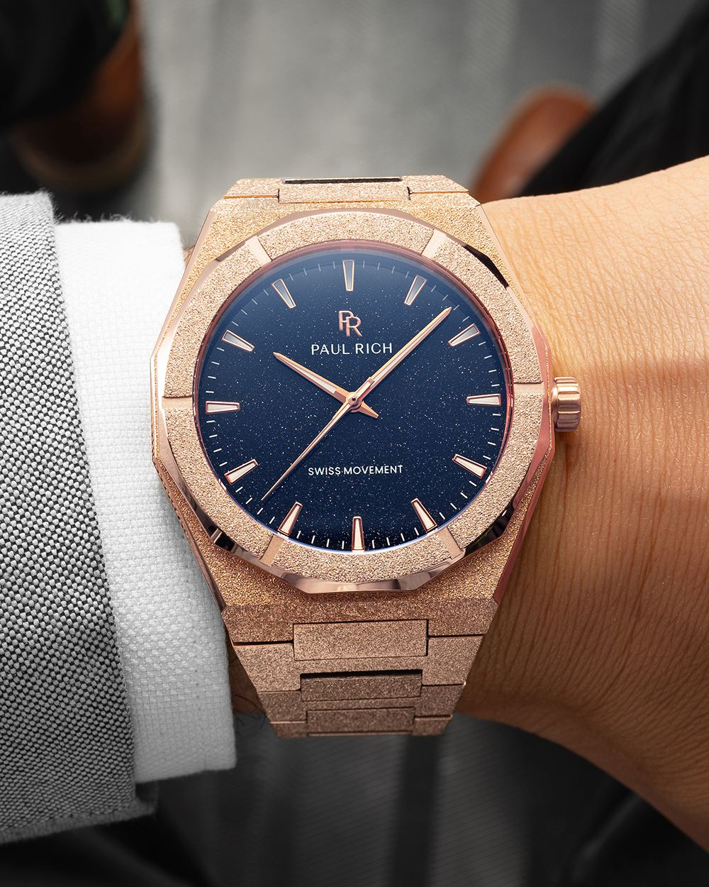 Rose gold frosted Paul Rich watch with deep blue aventurine dial worn on wrist, paired with a grey suit and white shirt cuff.