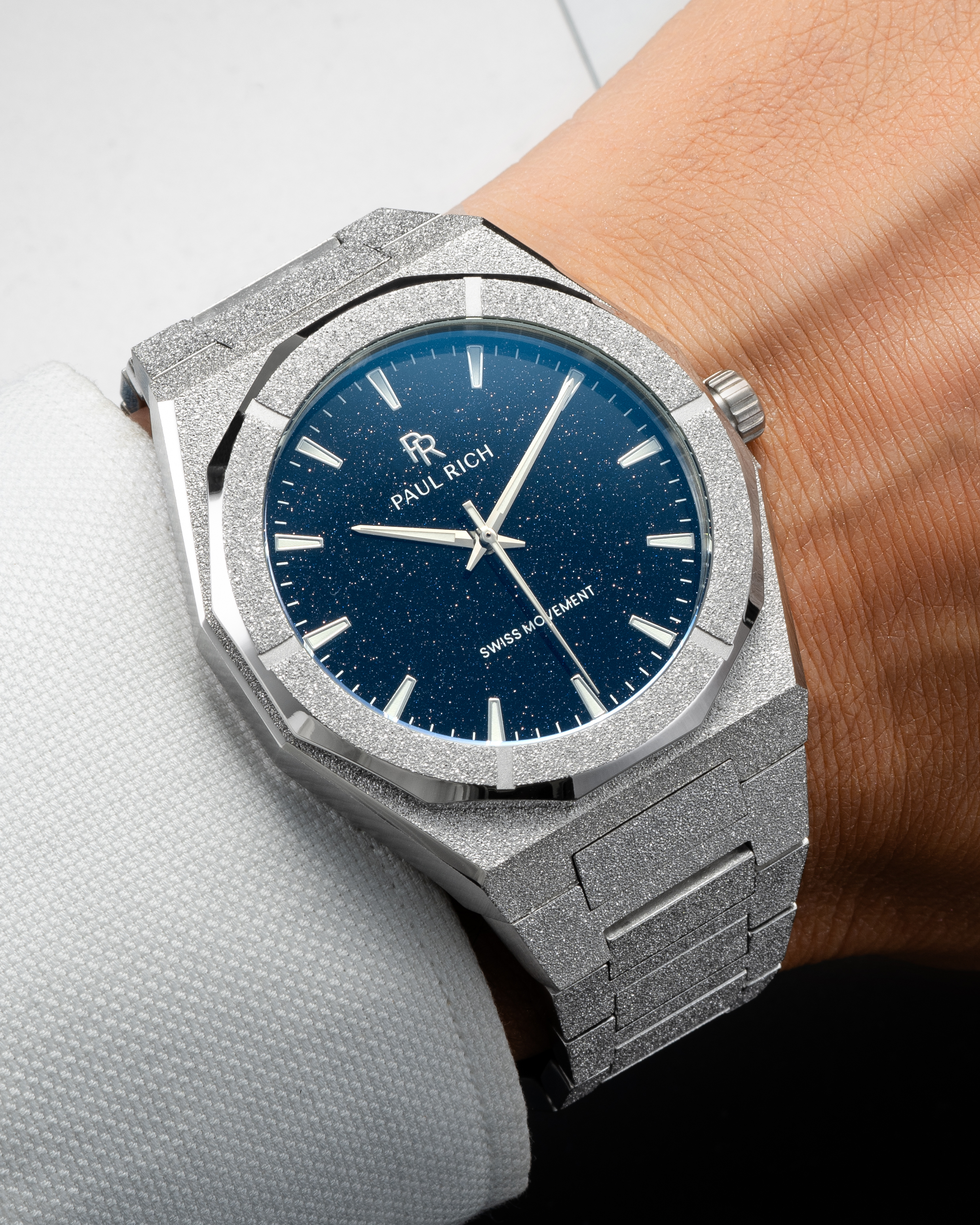 Silver frosted Paul Rich watch with blue aventurine dial worn on wrist, paired with a white textured dress shirt.