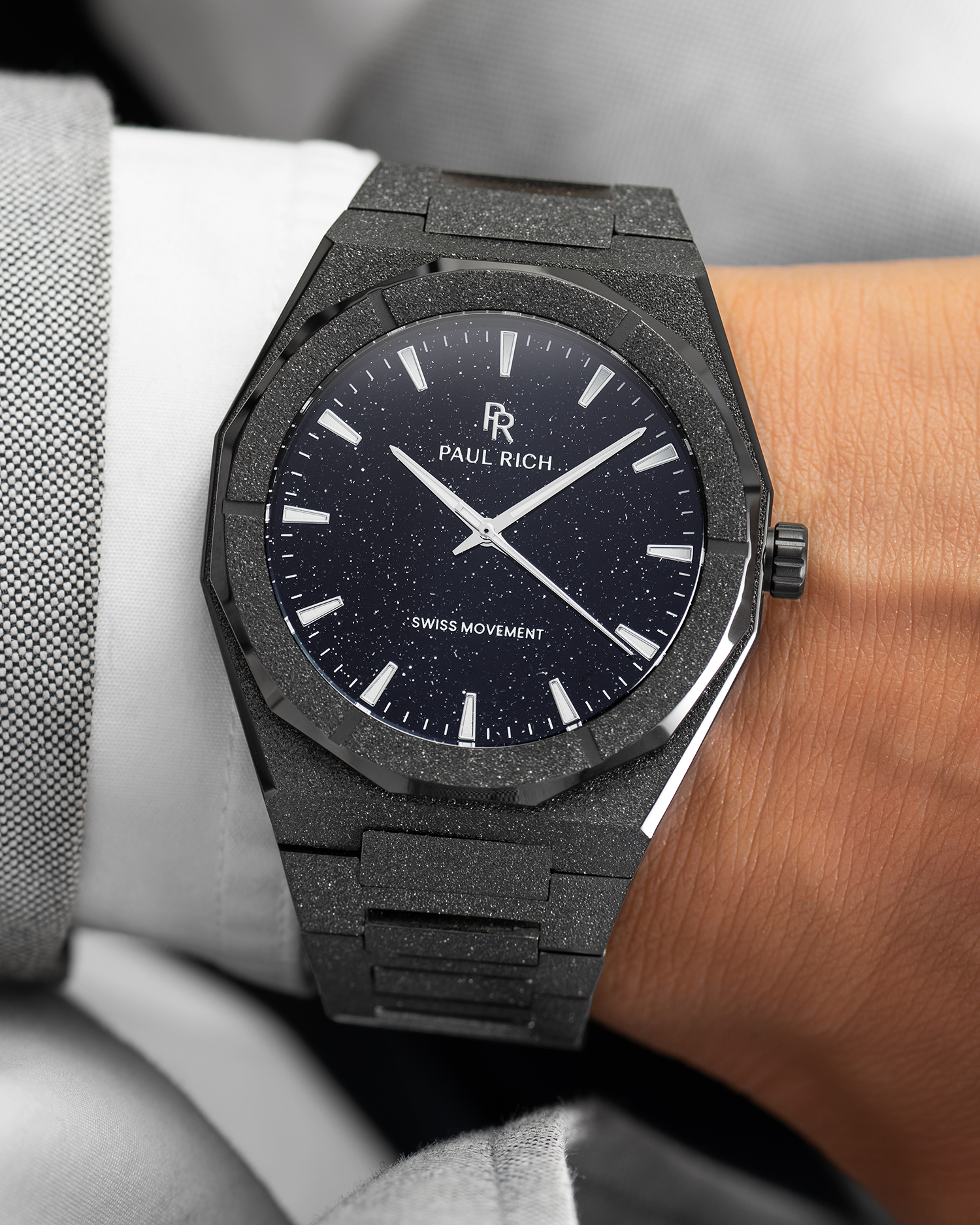 Paul Rich watch with frosted black case and black aventurine dial, worn on wrist with a white cuff and light grey textured suit.