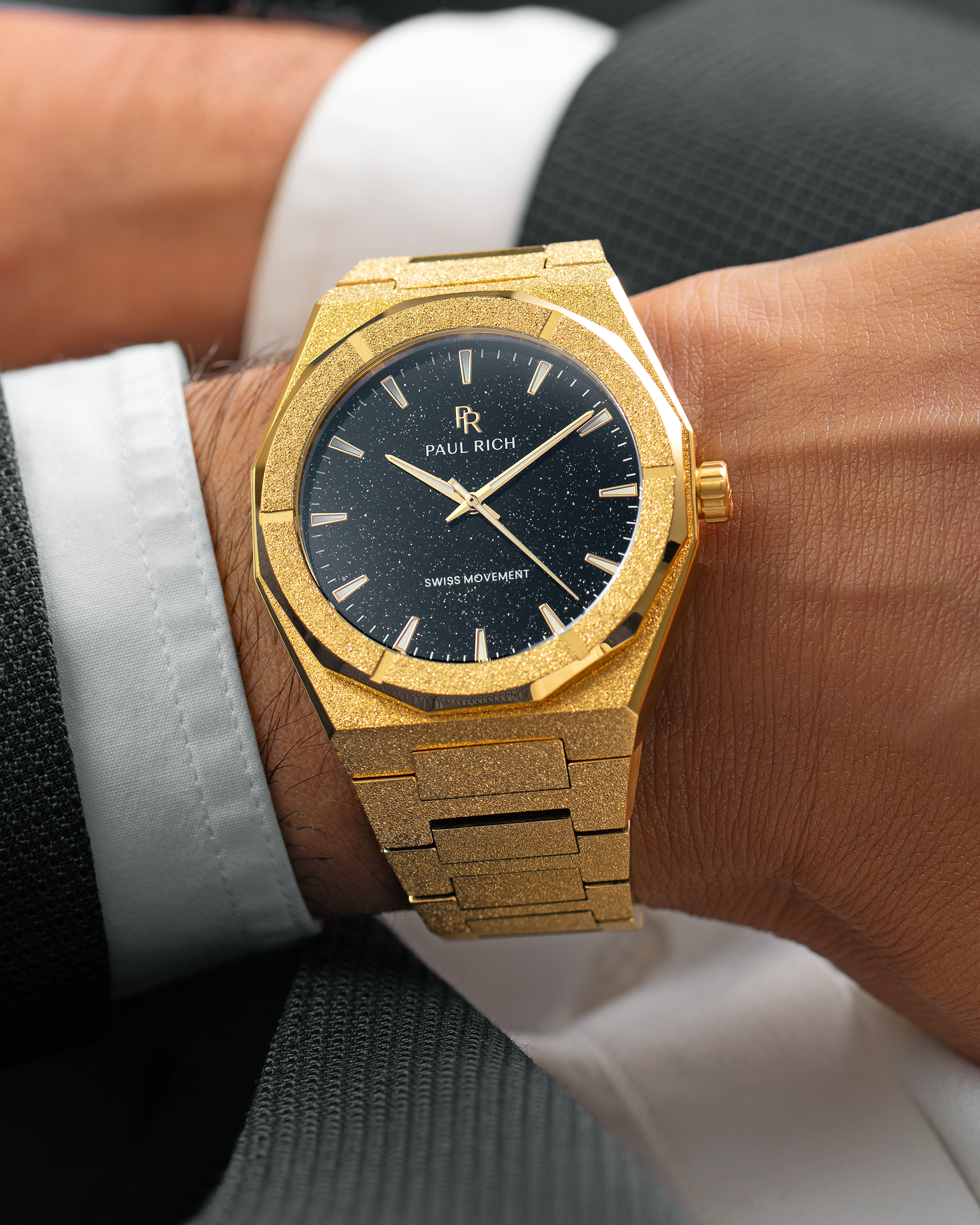 Gold Paul Rich watch with black aventurine dial and frosted finish, worn on wrist with a suit jacket and white cuff.