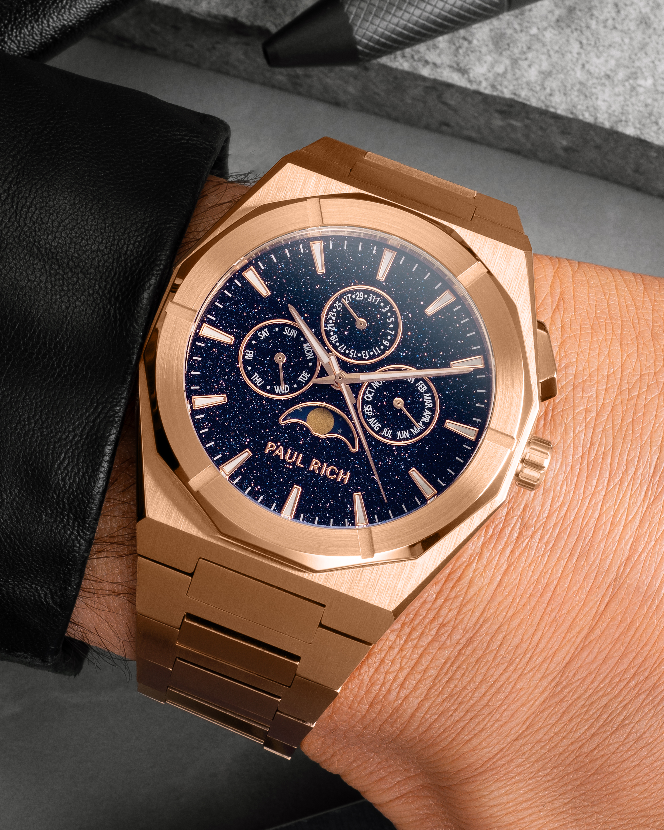 Rose gold moonphase watch on wrist with aventurine dial, day, date, and month subdials, brushed rose gold bracelet.