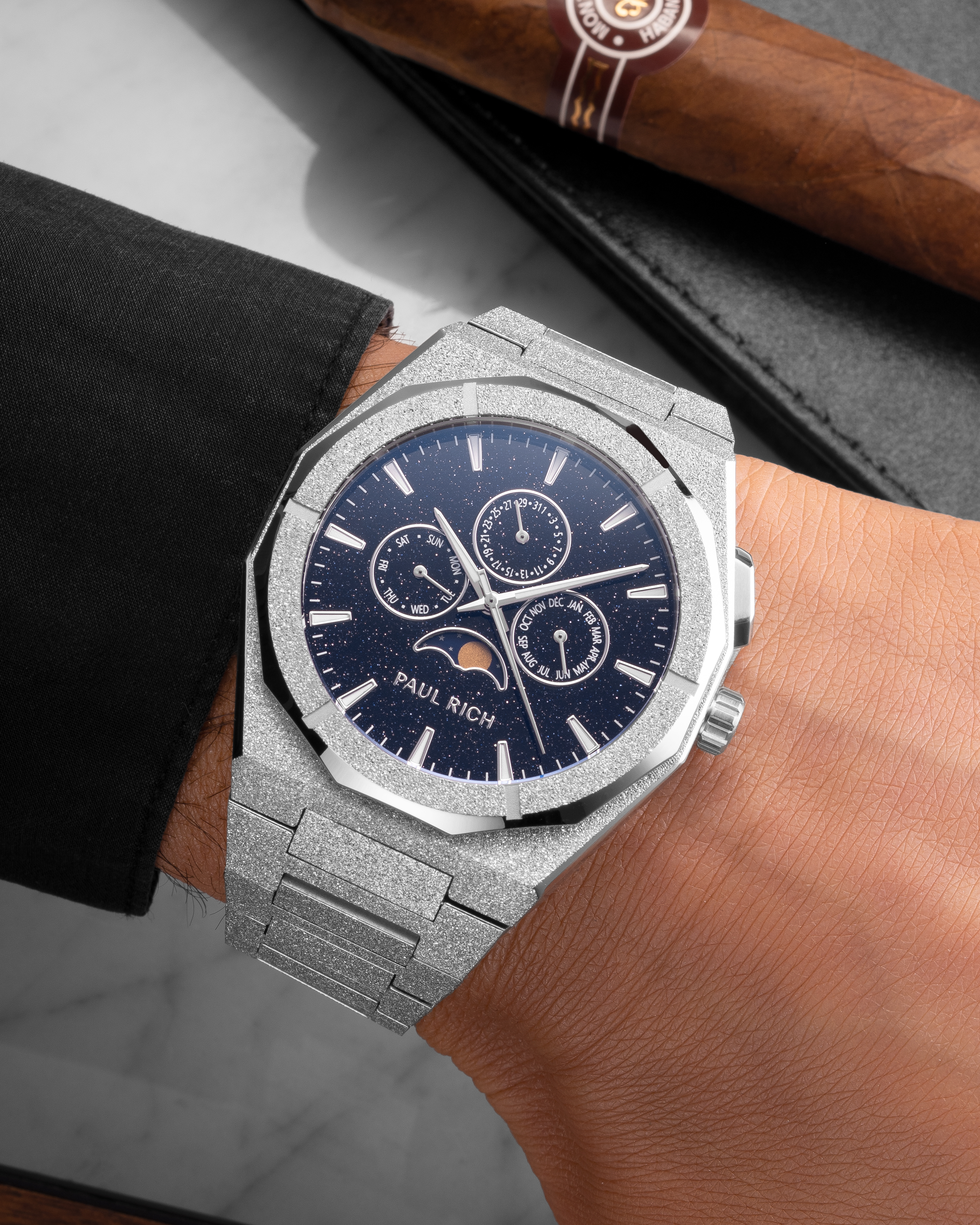Frosted silver moonphase watch on wrist with blue aventurine dial, calendar subdials, and textured silver bracelet.