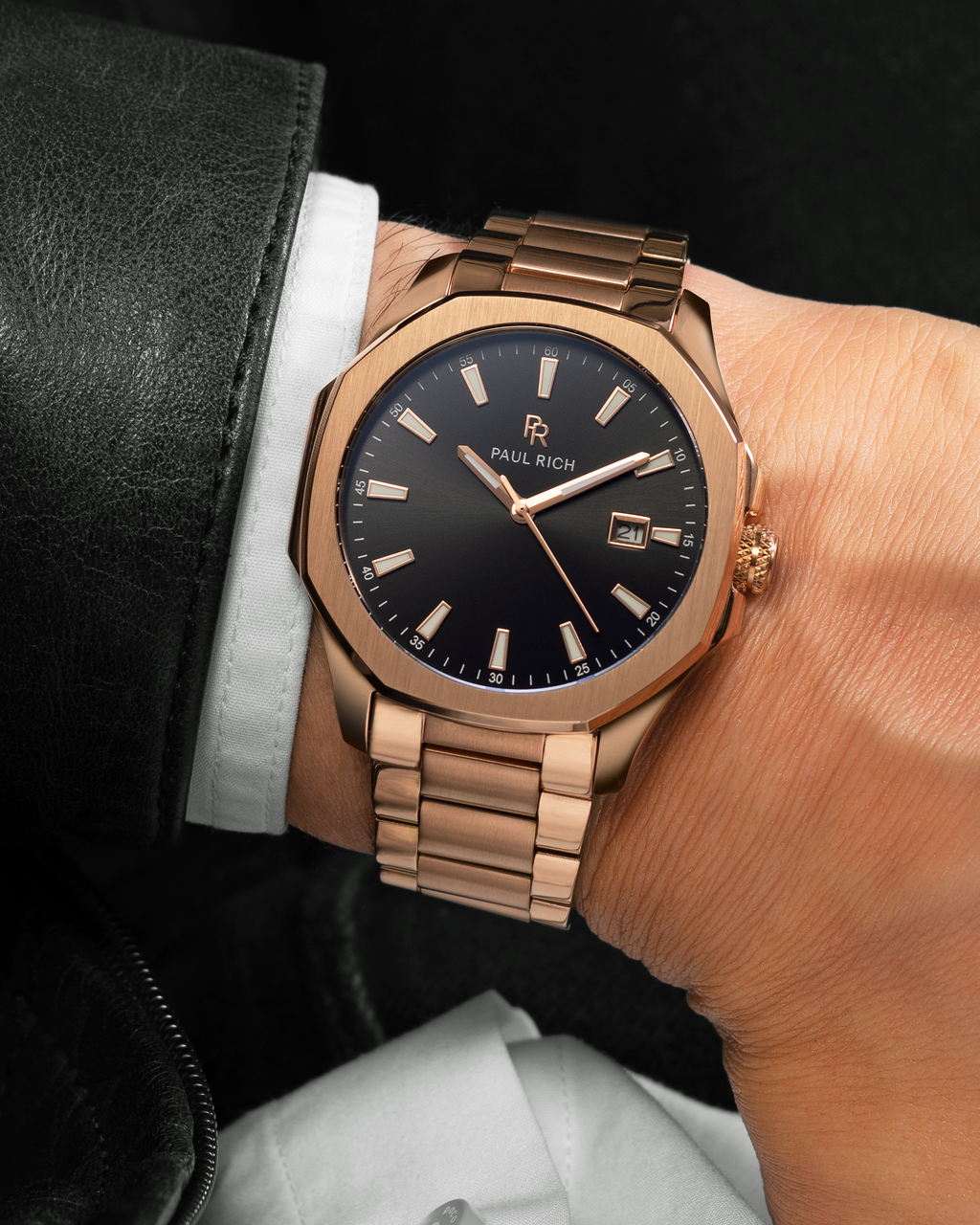 Rose gold Paul Rich watch with black sunray dial, steel bracelet, and date window, shown on wrist with white shirt and black leather jacket.