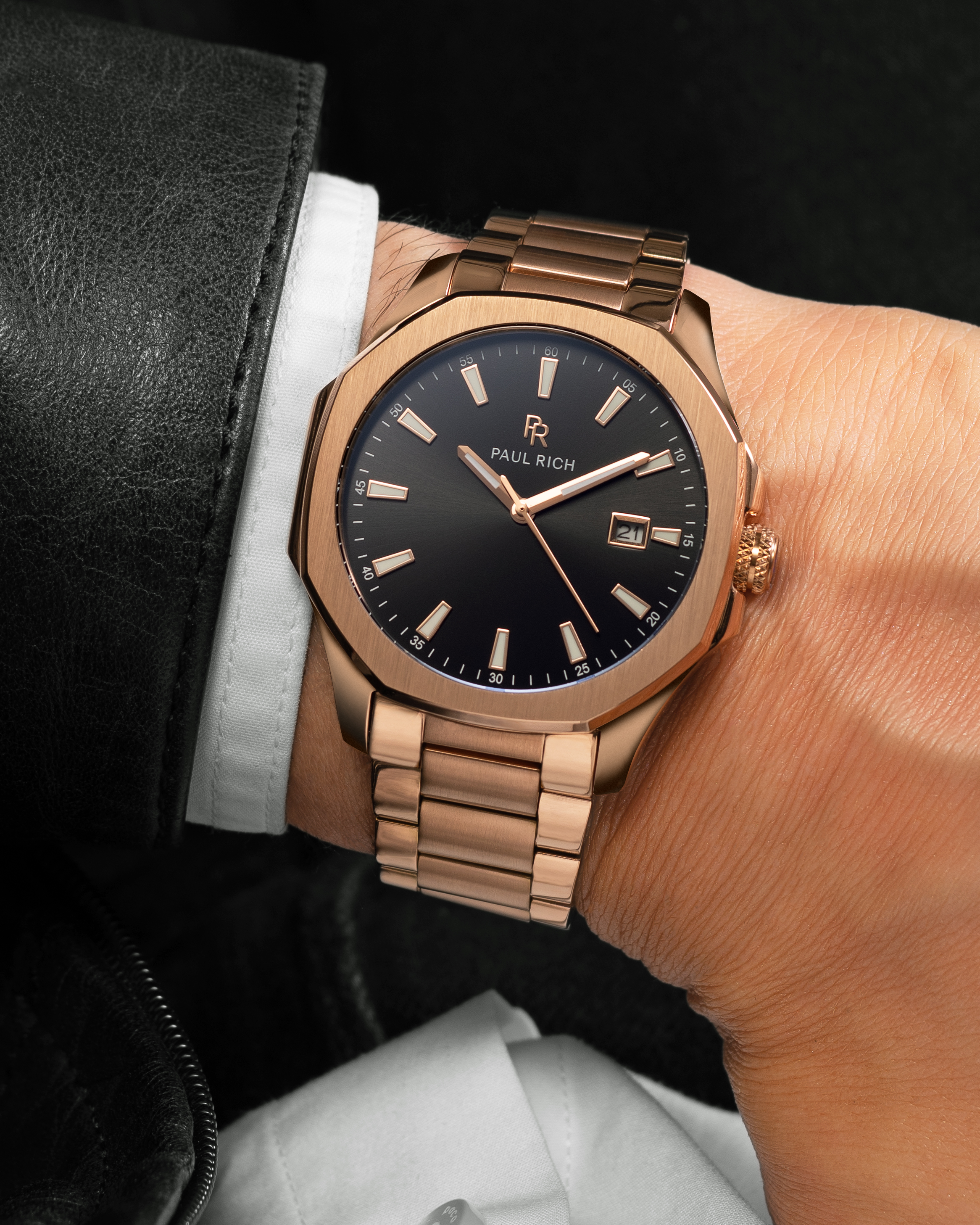Rose gold Paul Rich watch with black sunray dial, steel bracelet, and date window, shown on wrist with white shirt and black leather jacket.