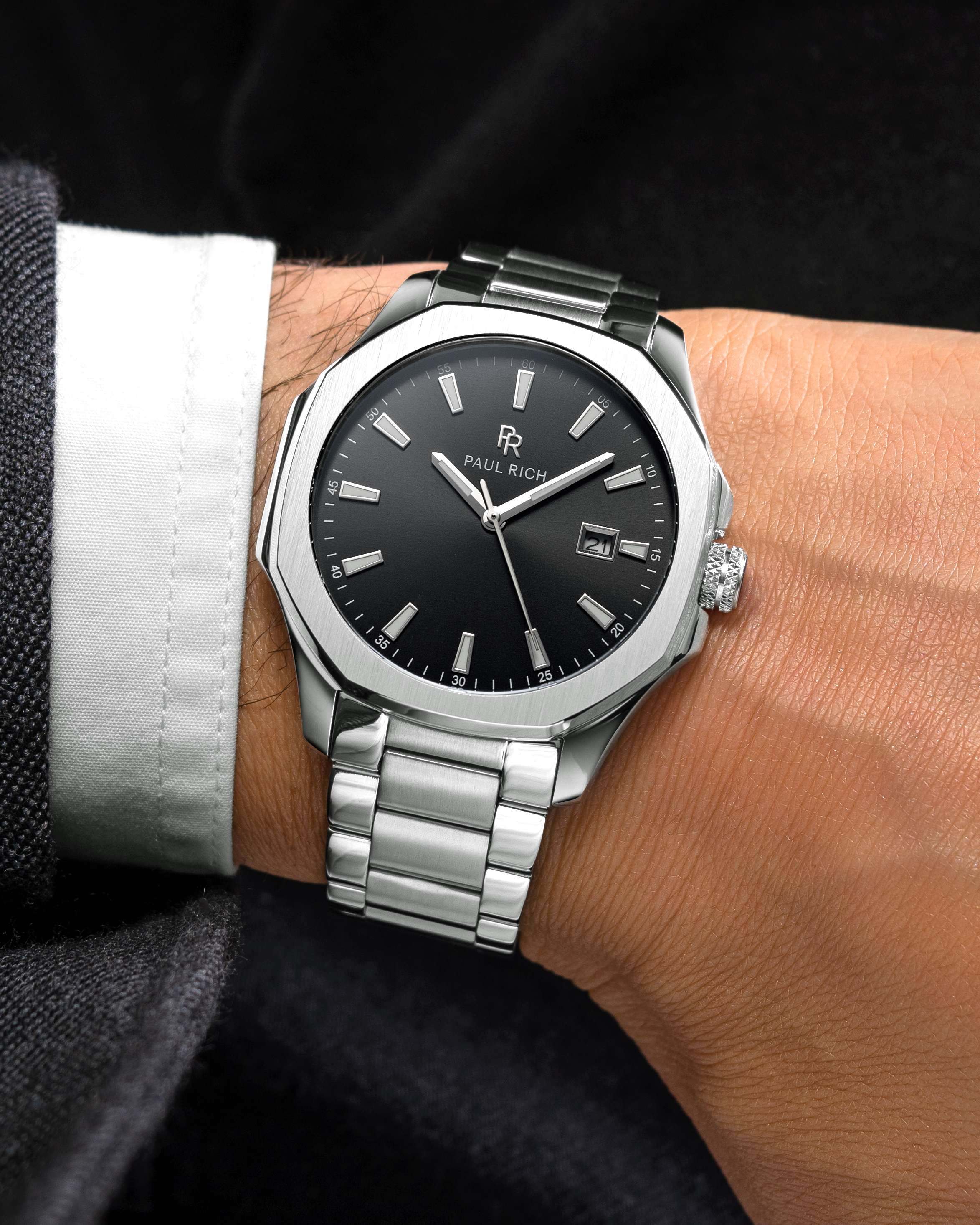 Silver Paul Rich watch with black sunray dial, steel bracelet, date window, and bold markers on a suited man's wrist.