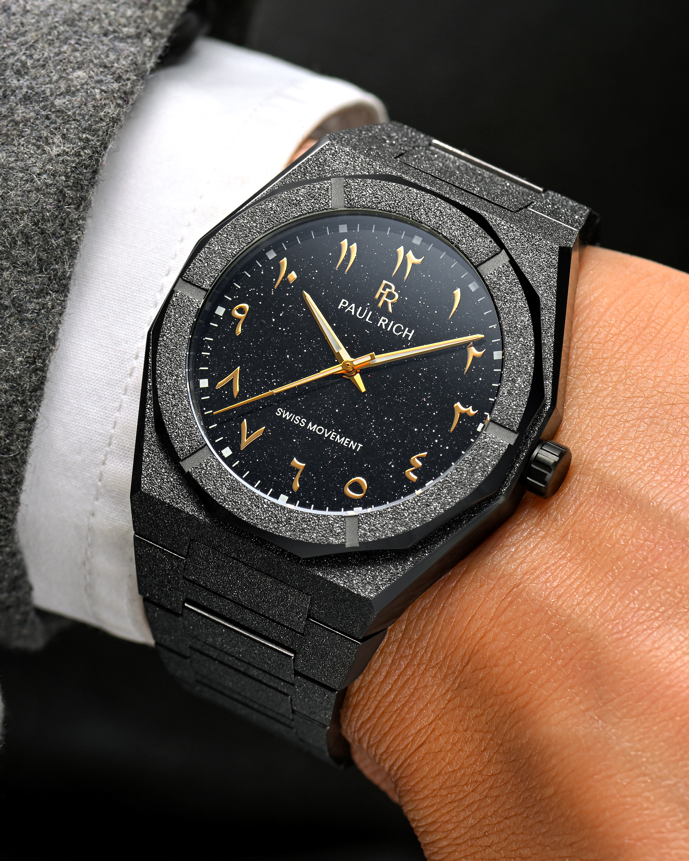 Close-up of Paul Rich frosted black watch with gold Arabic numerals and black aventurine dial, worn.