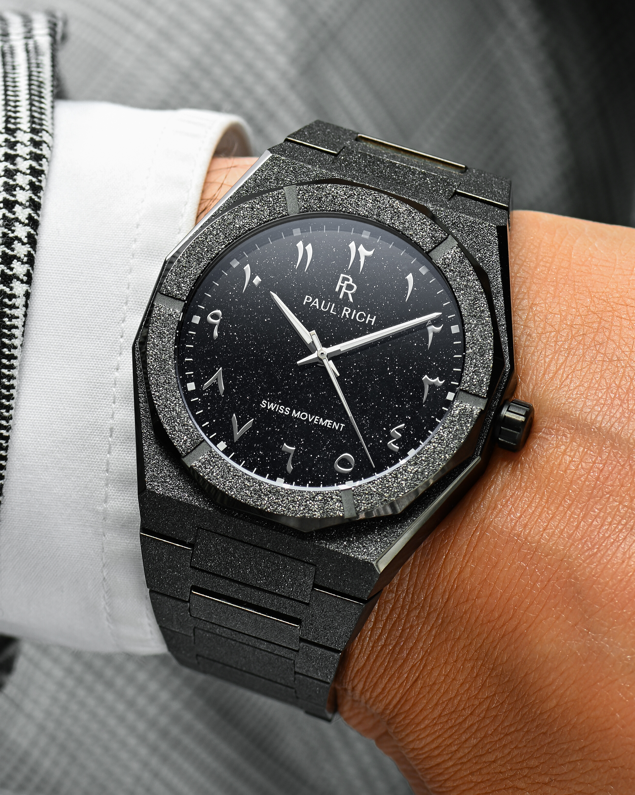 Close-up of Paul Rich frosted black watch with silver Arabic numerals and black aventurine dial, worn with white shirt and houndstooth jacket.
