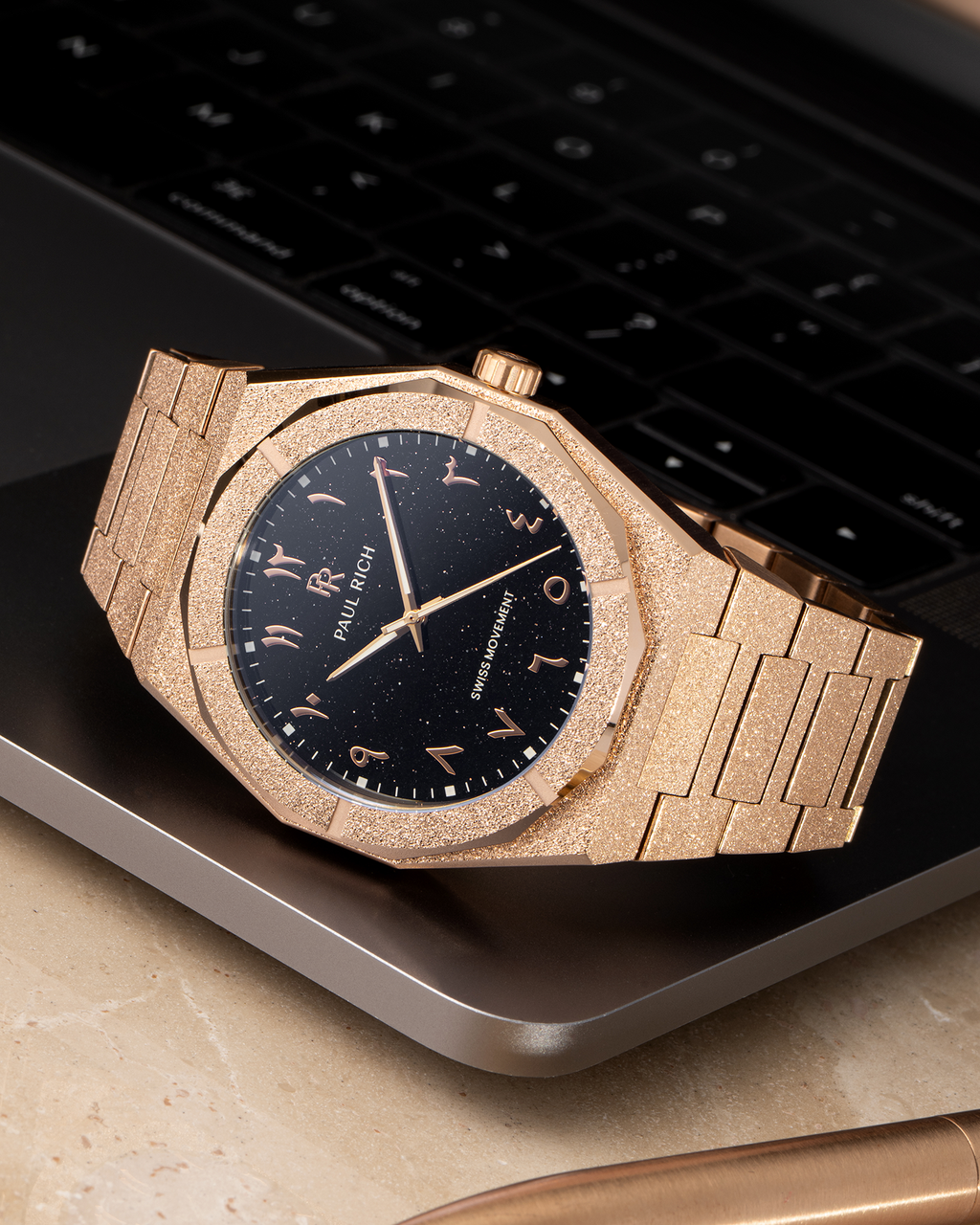 Paul Rich frosted rose gold watch with black aventurine dial and rose gold Arabic numerals, resting on a MacBook corner.