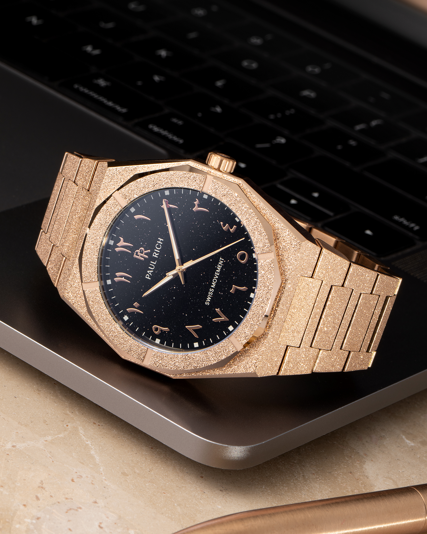 Paul Rich frosted rose gold watch with black aventurine dial and rose gold Arabic numerals, resting on a MacBook corner.