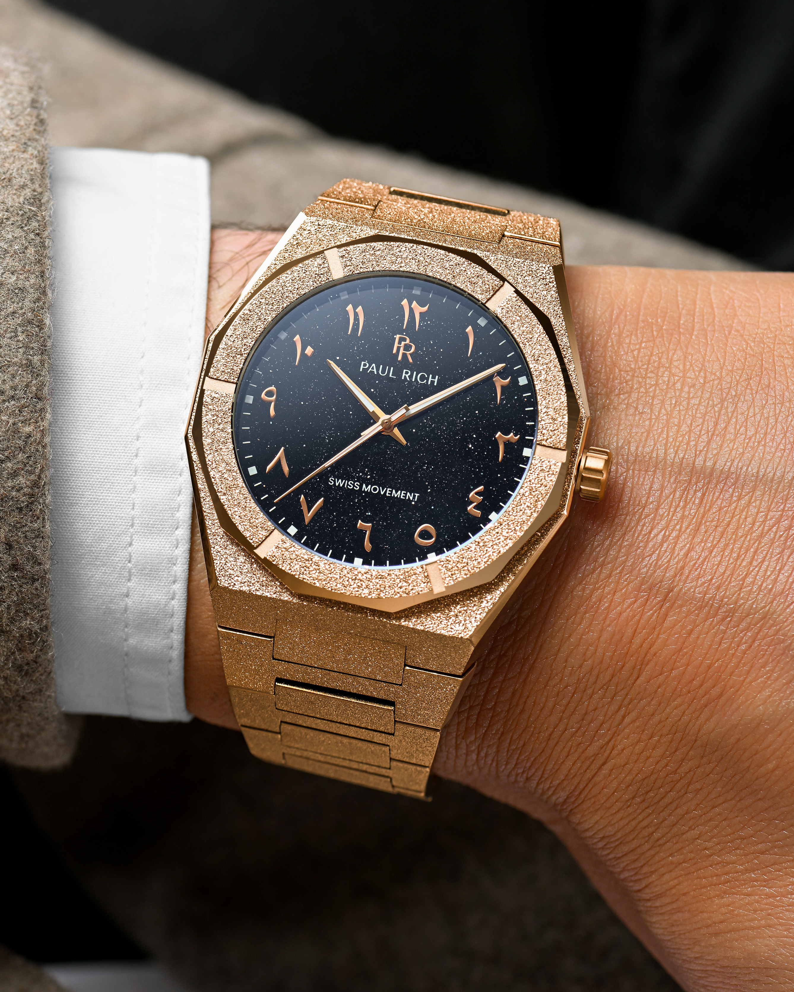 Close-up of Paul Rich rose gold frosted watch with Arabic numerals and black aventurine dial, shown on a wrist in formalwear.