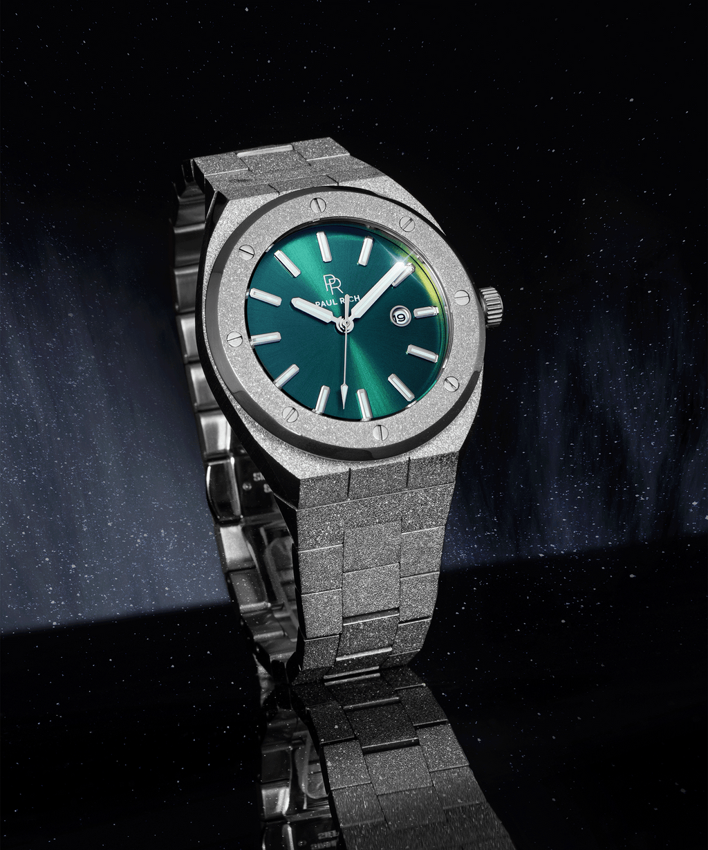 Paul Rich frosted watch with green sunray dial, silver markers, and date window, shown at an angle on a reflective black surface.