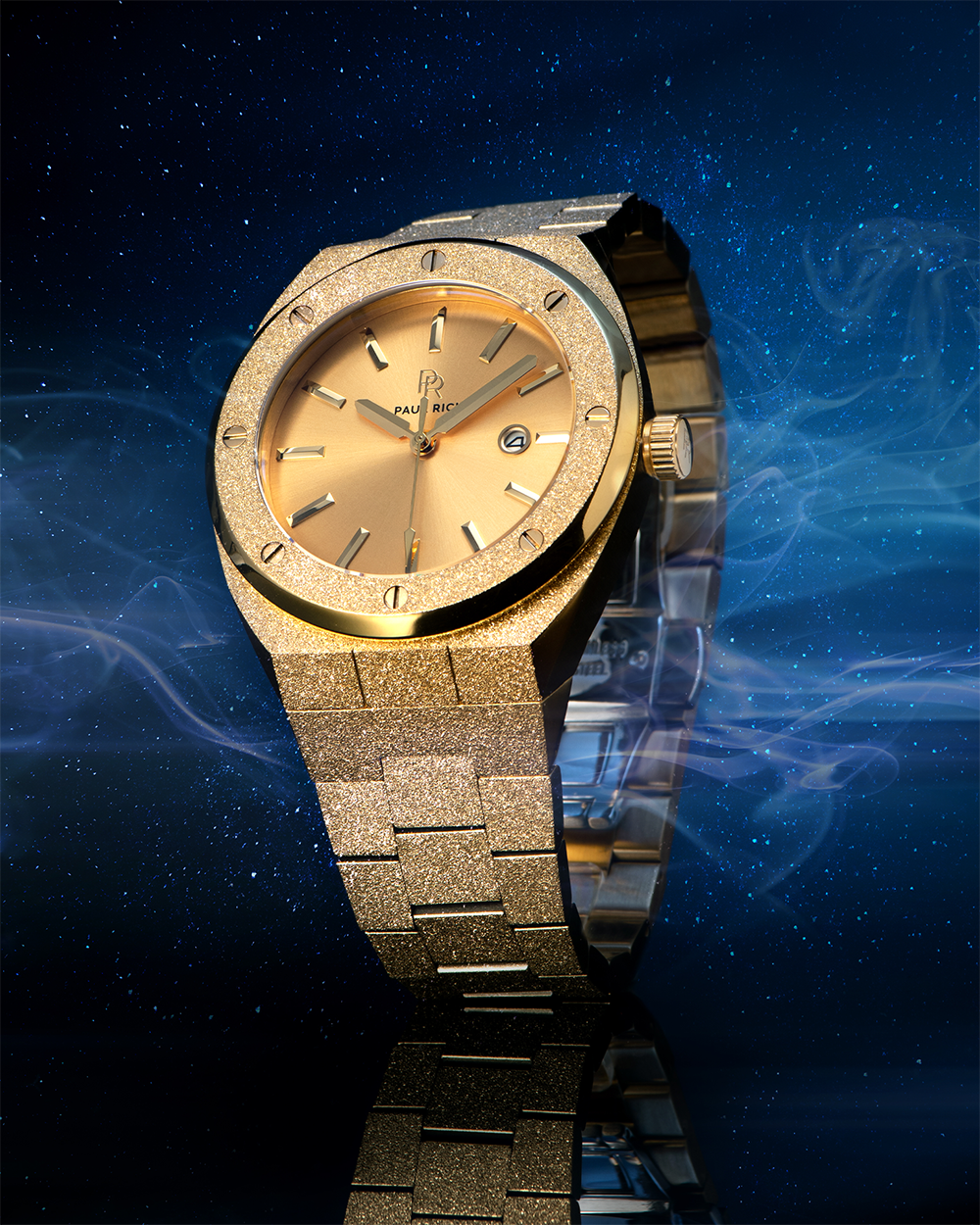Paul Rich watch with frosted gold case and bracelet, metallic champagne gold sunray dial, and date window, displayed against a starry night sky with mist.