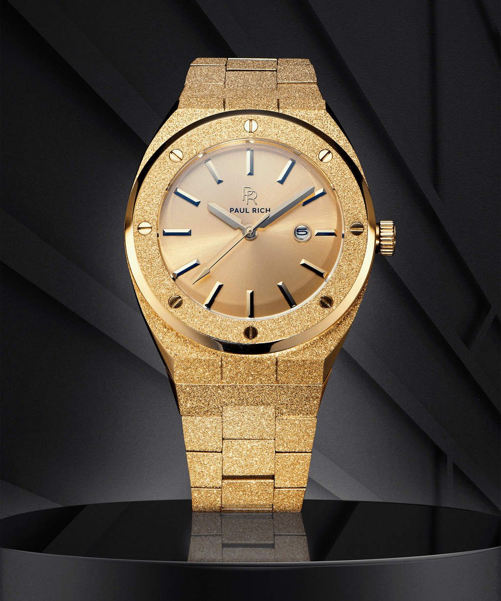 Paul Rich watch with frosted gold case and bracelet, metallic champagne gold sunray dial, and date window, displayed on a black geometric background.