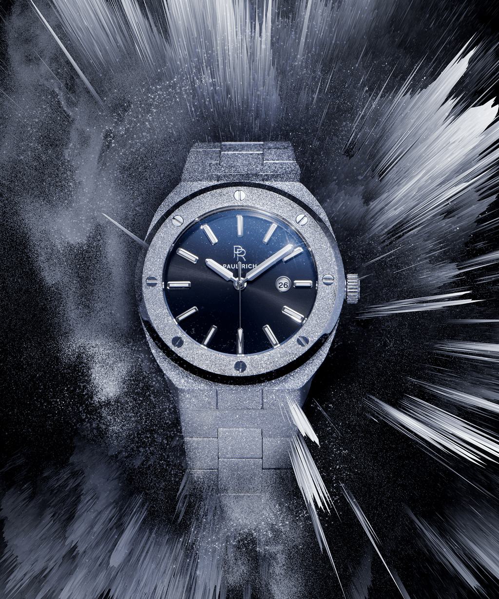 Paul Rich watch with frosted silver case and bracelet, metallic black sunray dial, and date window, displayed in a dynamic icy burst effect on dark background.