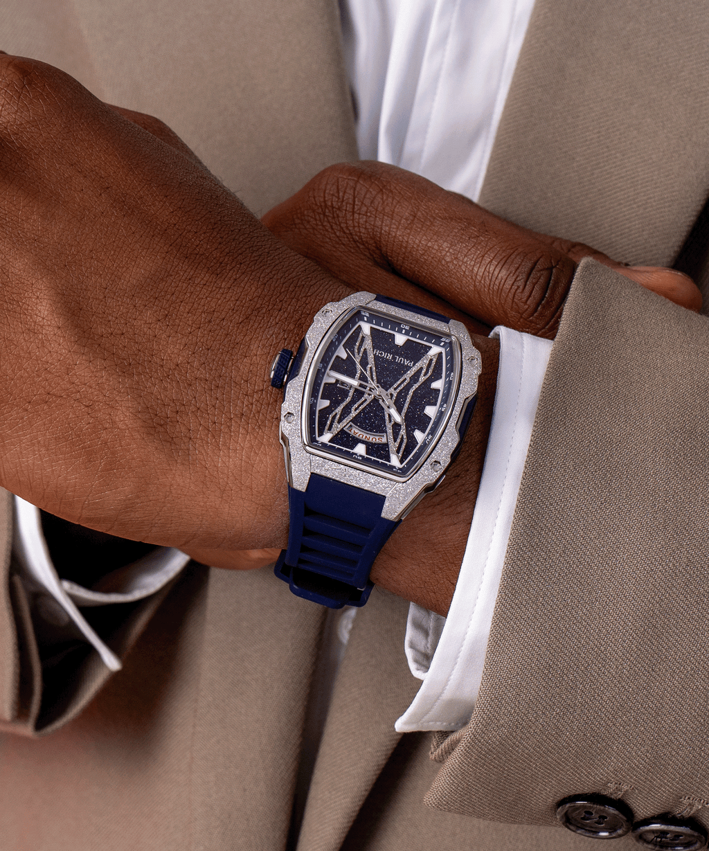 Paul Rich watch with blue aventurine dial, silver frosted bezel, and blue strap worn on wrist with beige suit and white shirt.
