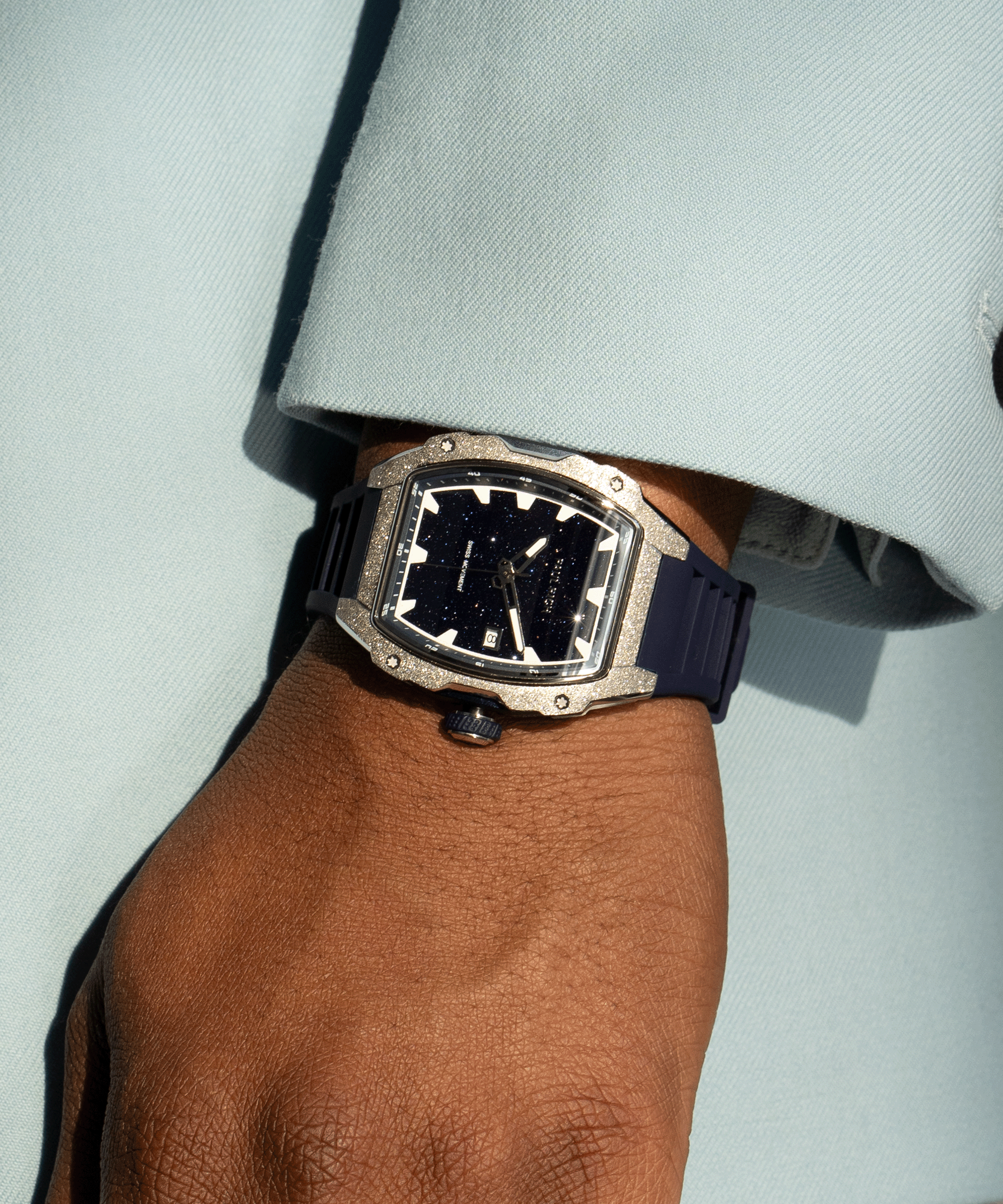 Paul Rich watch with tonneau case, frosted silver bezel, and blue aventurine dial, worn on wrist with light blue sleeve in sunlight.