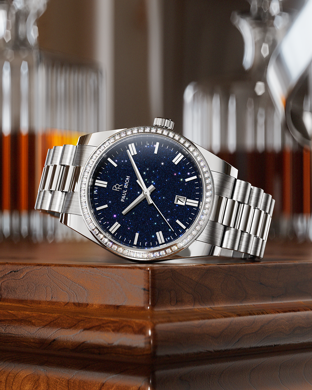Silver wristwatch with a blue speckled dial and crystal-set bezel resting on a polished wooden surface, with glass decanters in the background.