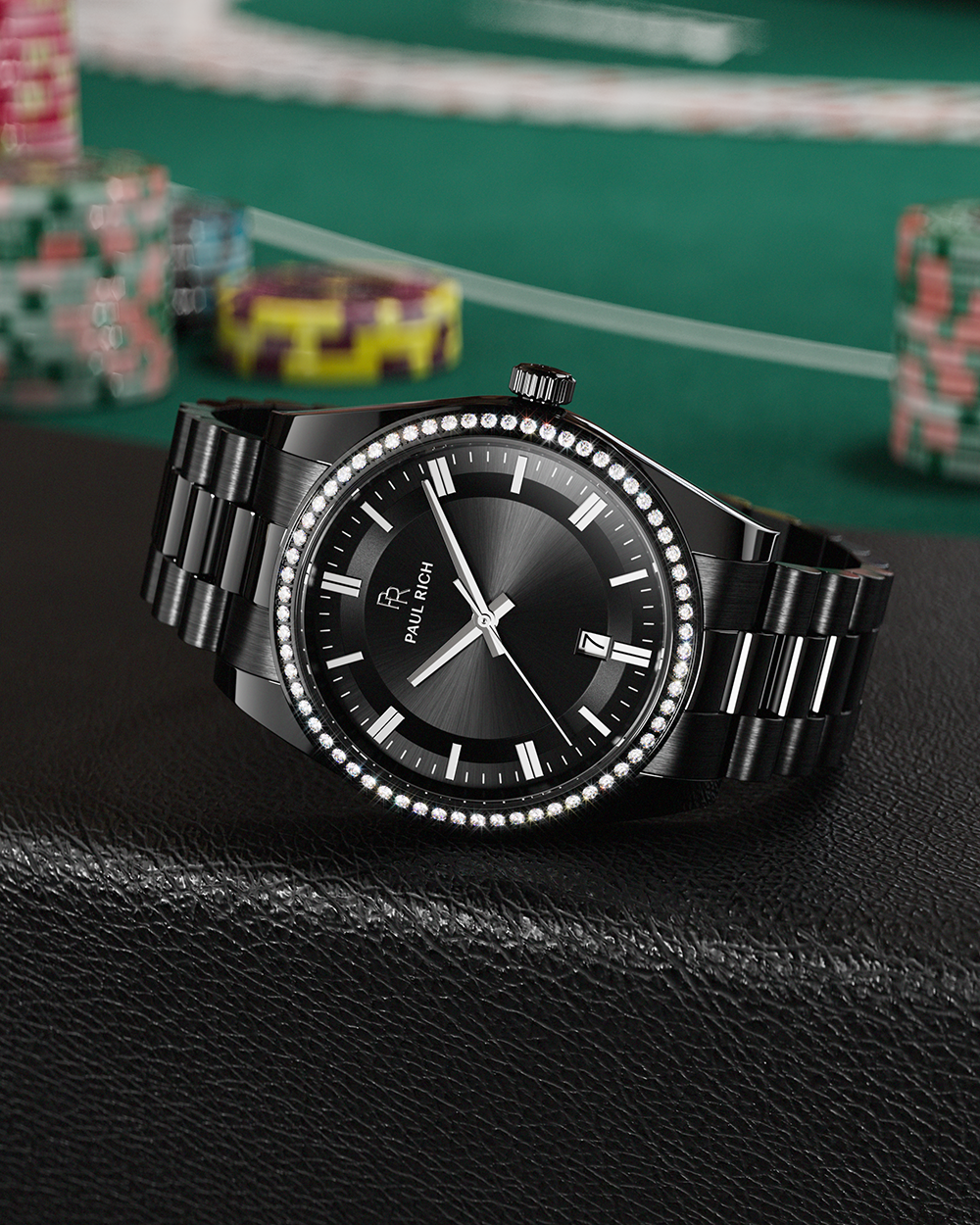 Black Paul Rich watch with black sunray dial, diamond-set bezel, and black link bracelet, displayed on a black leather surface with poker chips and a green casino table in the background.