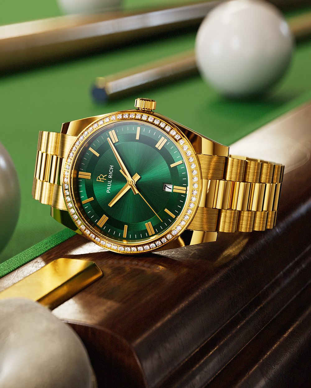Gold-tone Paul Rich watch with green sunray dial, diamond-set bezel, and gold link bracelet, displayed on the wooden edge of a pool table with billiard balls and cues in the background.