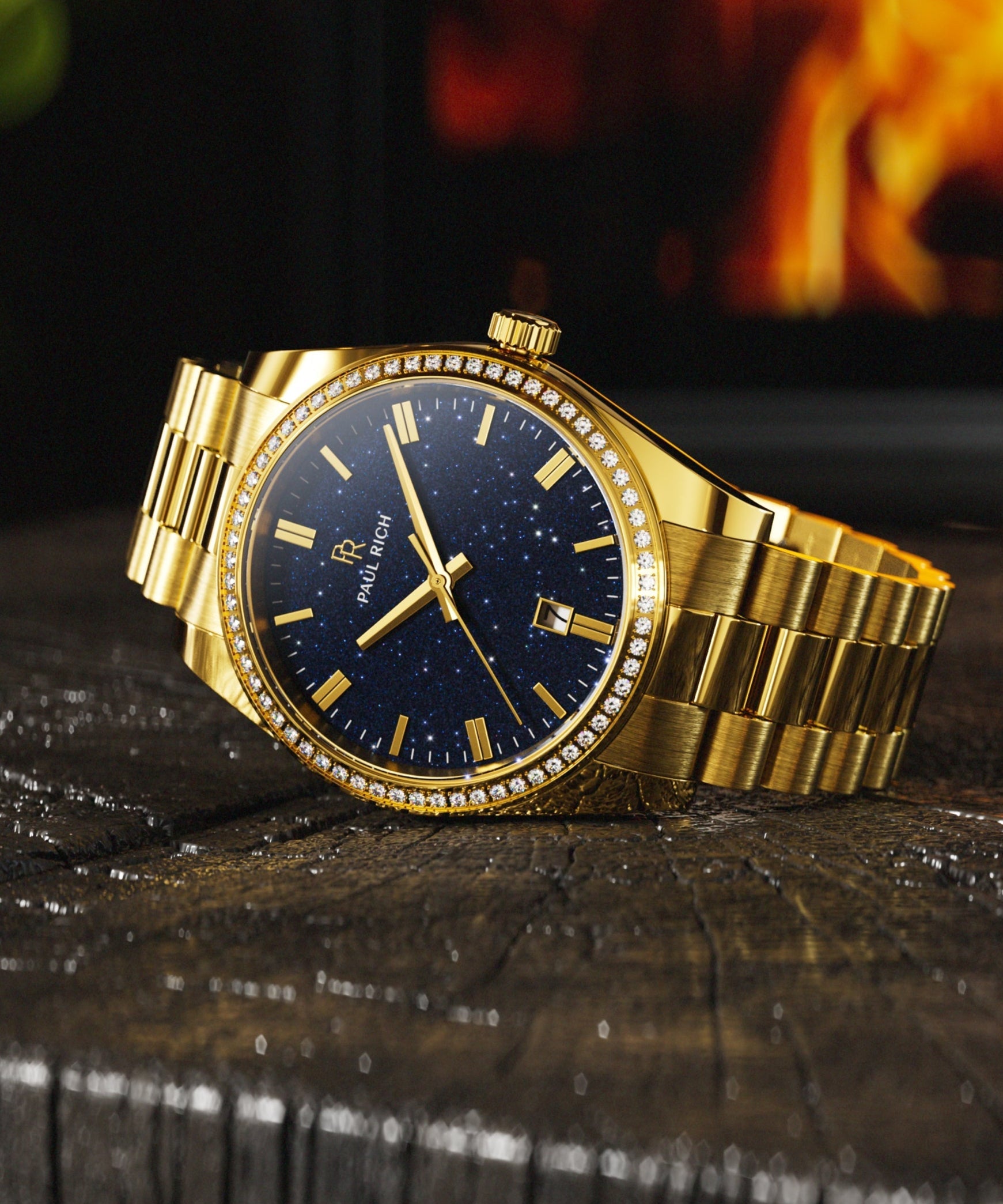 Gold Paul Rich watch with a blue aventurine dial and gem-set bezel, resting on wood with a fireplace glowing in the background.
