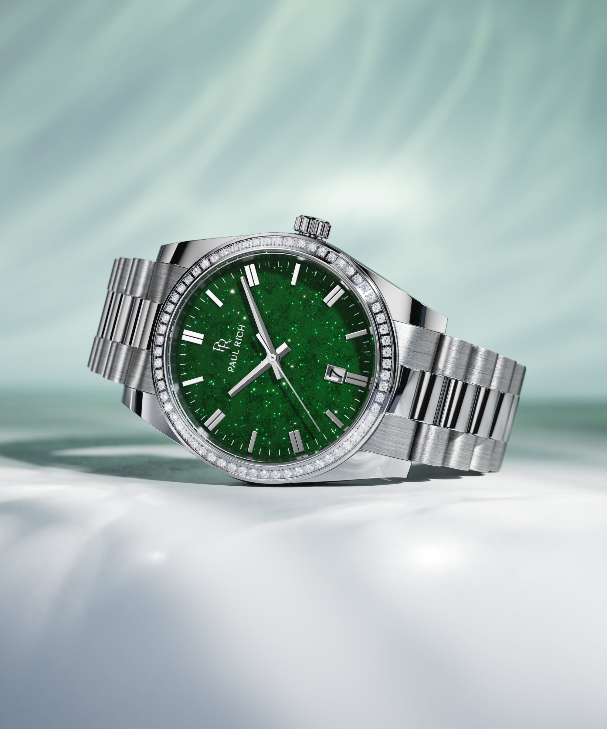 Silver wristwatch with a green aventurine dial, crystal-set bezel, and metal bracelet displayed on a white surface with soft green lighting.