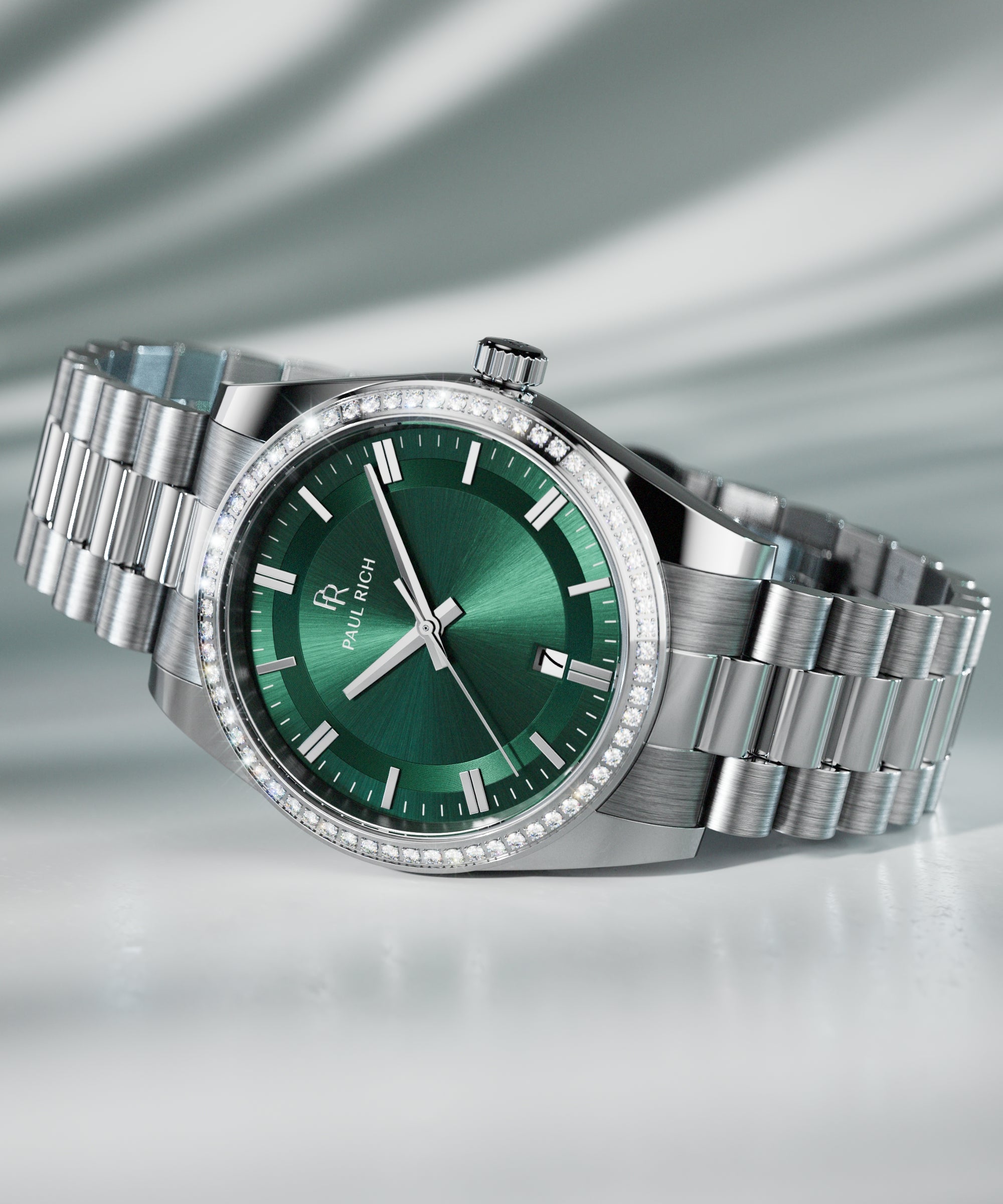 Silver wristwatch with a green sunburst dial, crystal-set bezel, and metal bracelet displayed on a reflective surface with soft lighting.