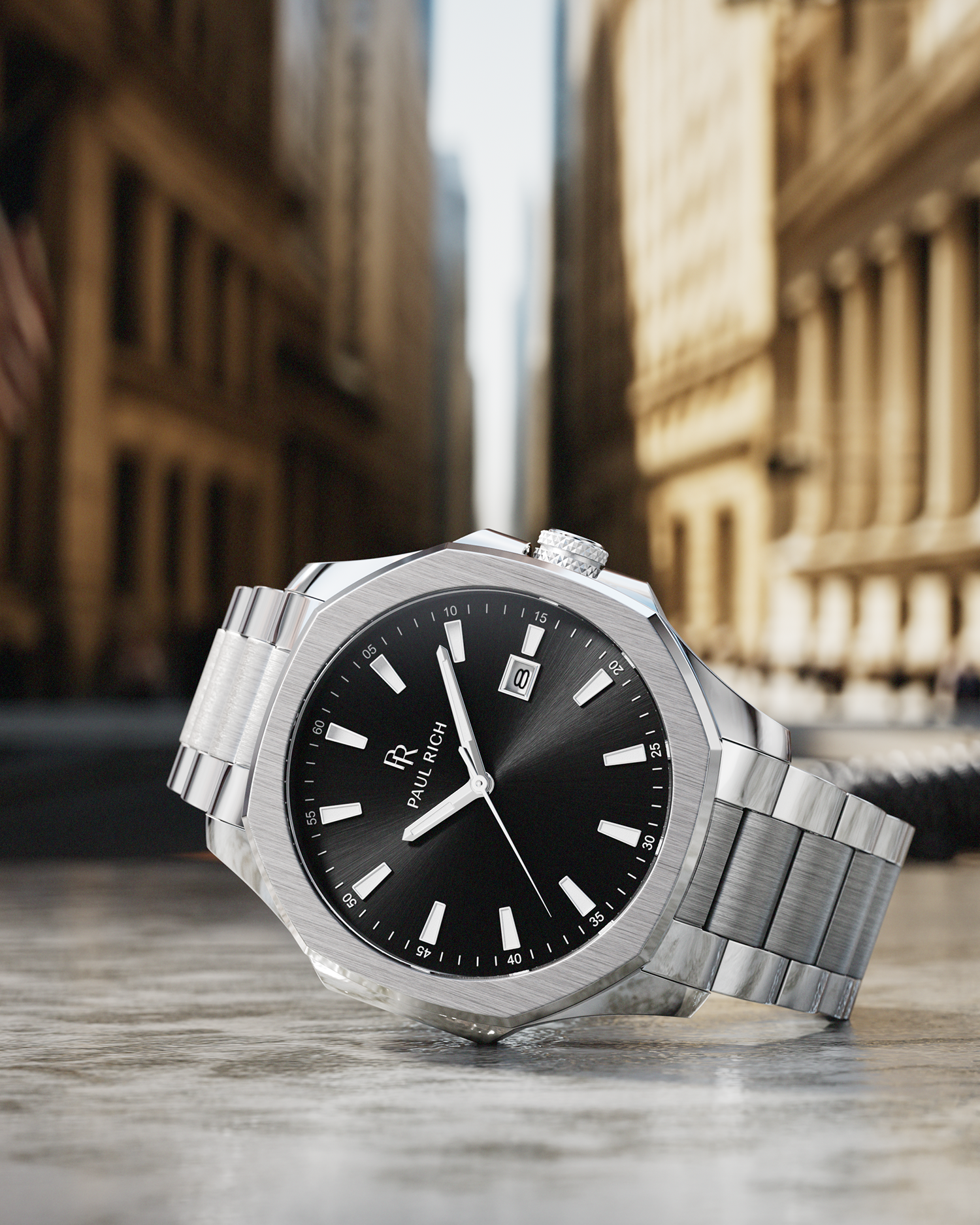 Paul Rich silver watch with black sunray dial and steel bracelet, photographed close-up on Wall Street with skyscrapers in background.