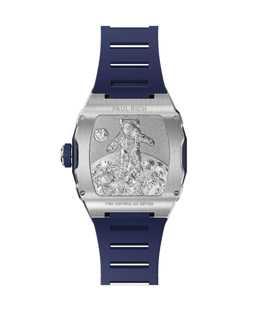 Back of Paul Rich tonneau-shaped watch showing engraved astronaut on lunar surface with 'PER ASPERA AD ASTRA' and blue rubber strap.