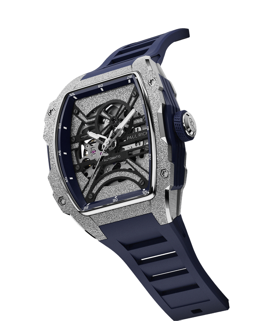 Angled view of Paul Rich watch with frosted silver tonneau case, skeleton dial, white hands, and blue rubber strap, shown on transparent background.