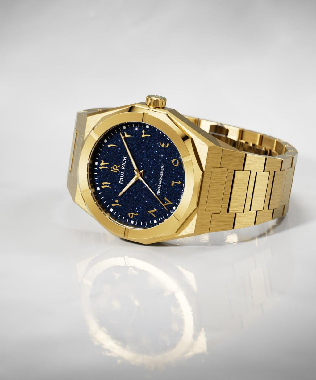 Paul Rich watch with brushed gold case and bracelet, blue aventurine dial with Arabic numerals, displayed on a glossy white surface.