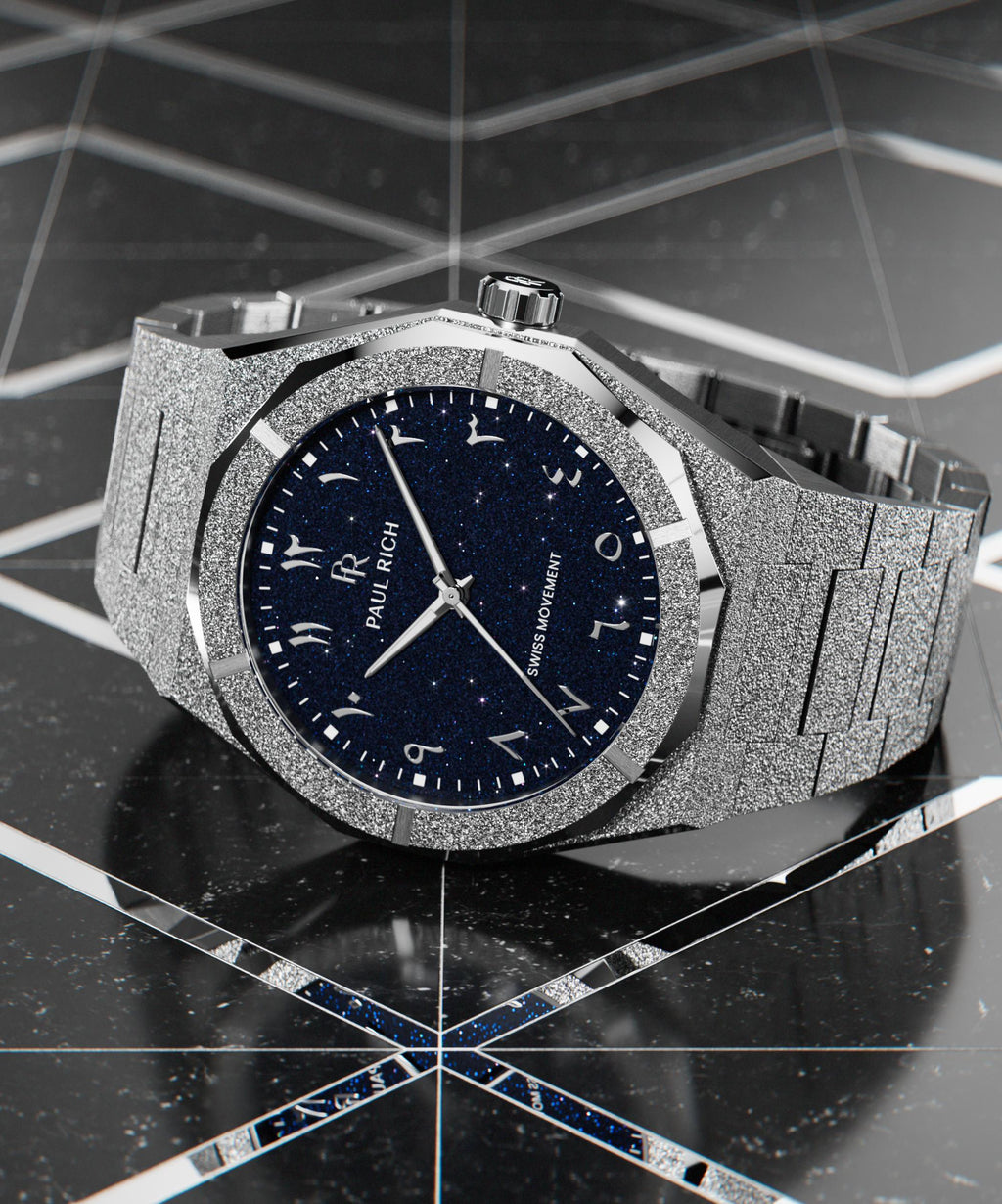 Frosted silver watch with a blue aventurine dial and Arabic numerals, displayed on a glossy black geometric surface with mirrored accents.