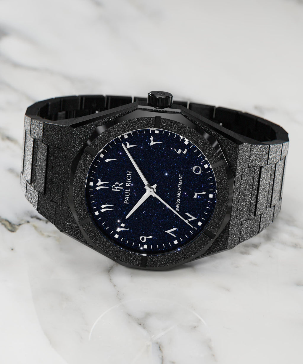 Frosted black watch with blue aventurine dial and Arabic numerals, displayed on a white marble surface.