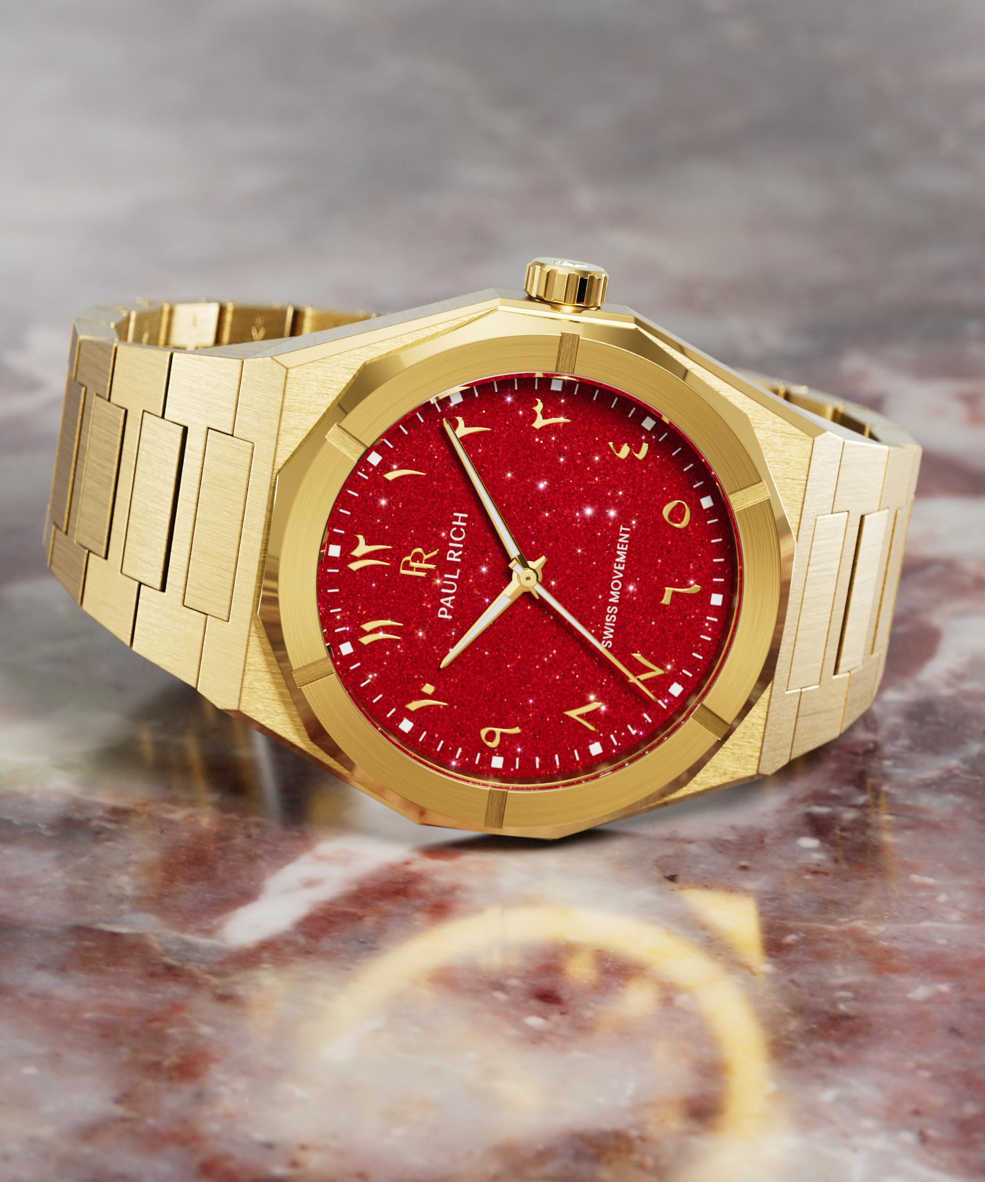 Paul Rich watch with brushed gold case and red aventurine dial featuring Arabic numerals, displayed on a polished red marble surface.