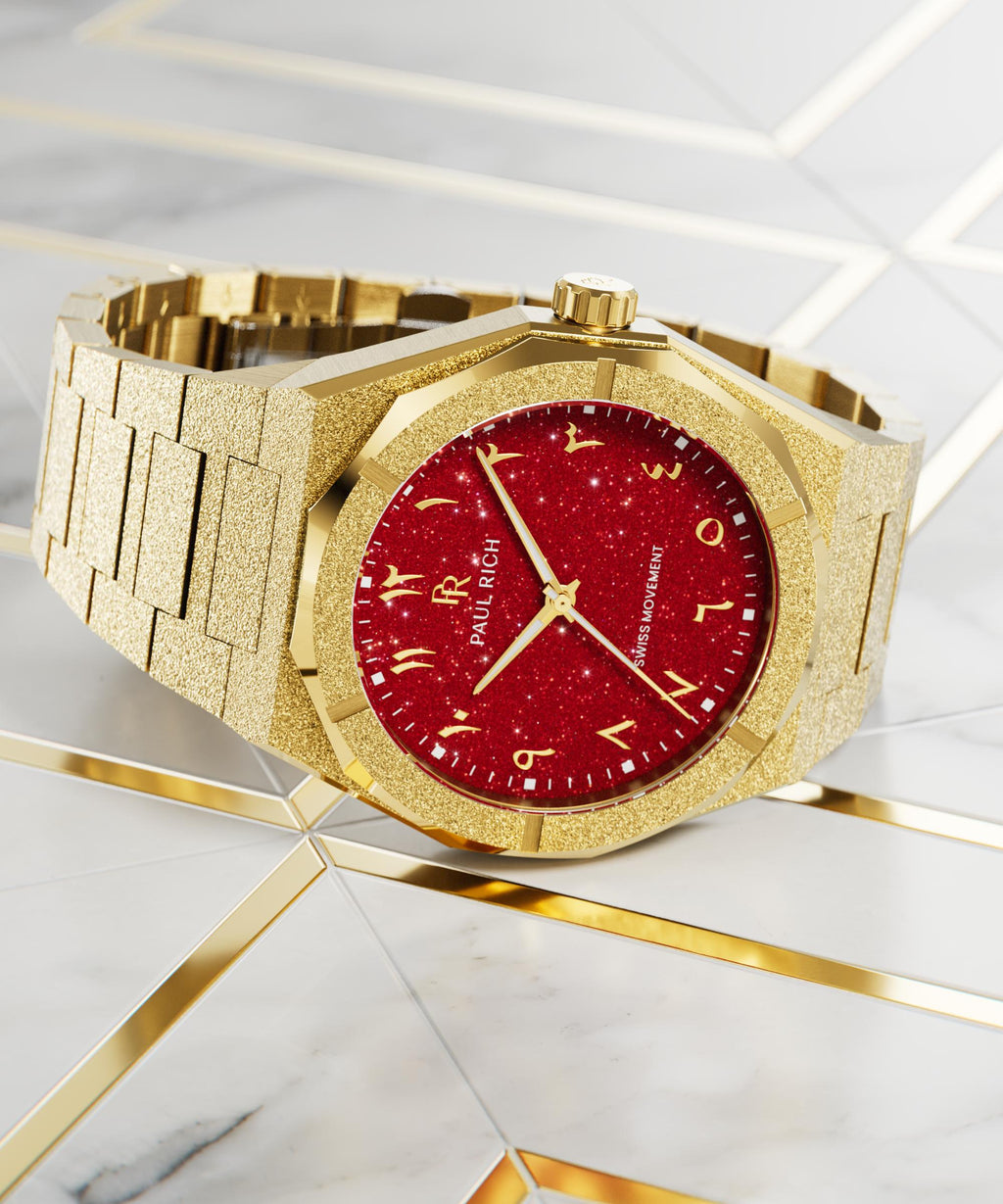 Paul Rich watch with frosted gold case and red aventurine dial with Arabic numerals, displayed on a marble and gold geometric surface.