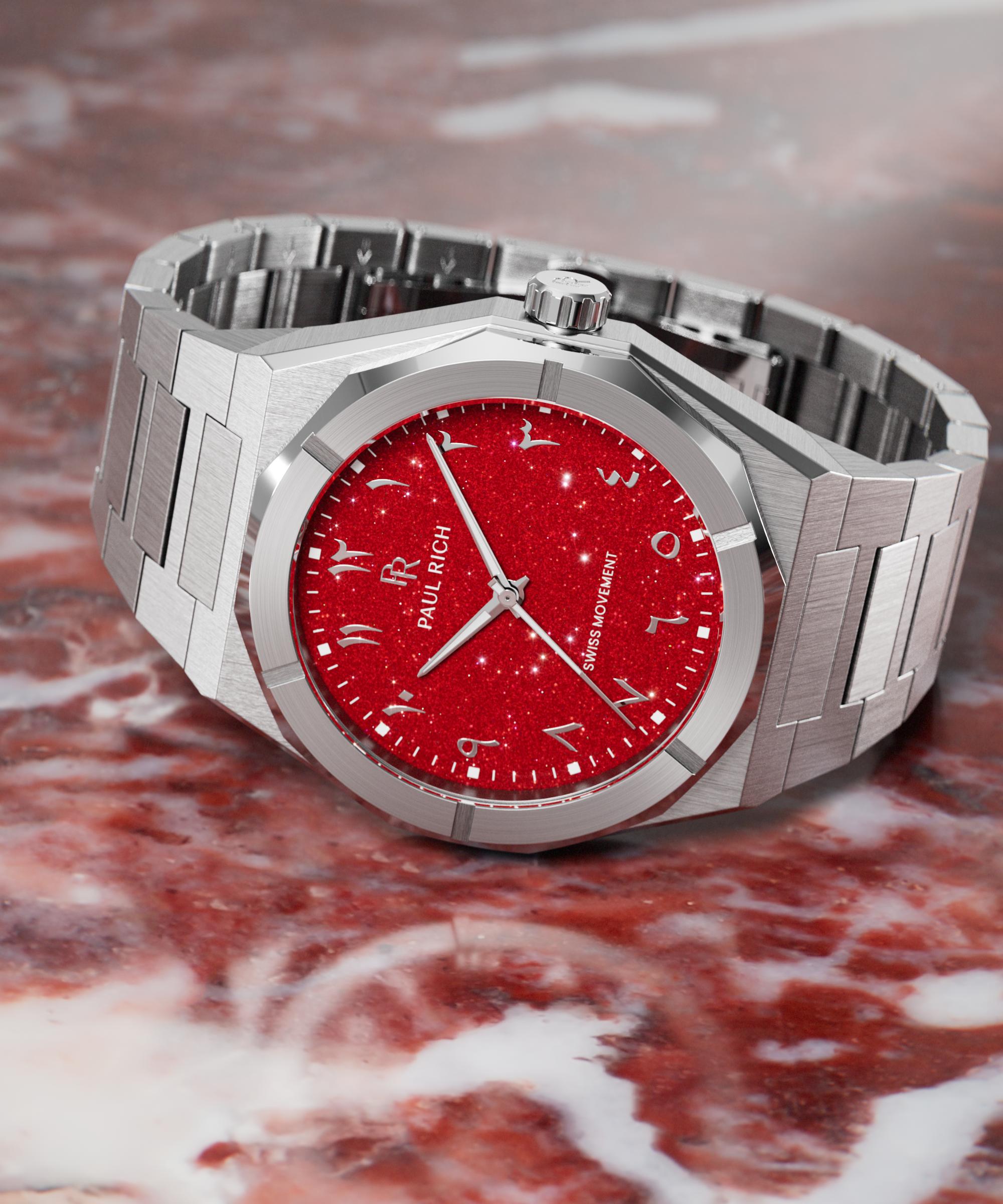 Paul Rich watch with brushed silver case and sparkling red dial featuring Arabic numerals, displayed on a polished red marble surface.