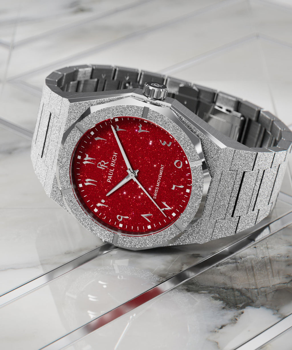 Paul Rich watch with frosted silver case and red aventurine dial with Arabic numerals, displayed on a polished white marble surface.