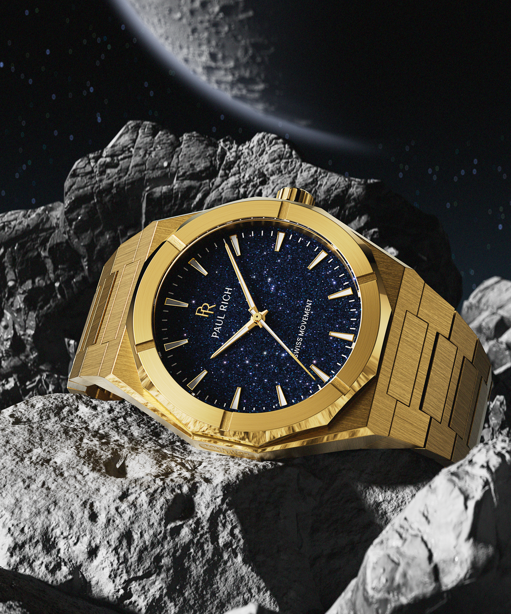 Gold Paul Rich watch with deep blue aventurine dial resting on rocky asteroid surface, with a large moon and stars in the background.