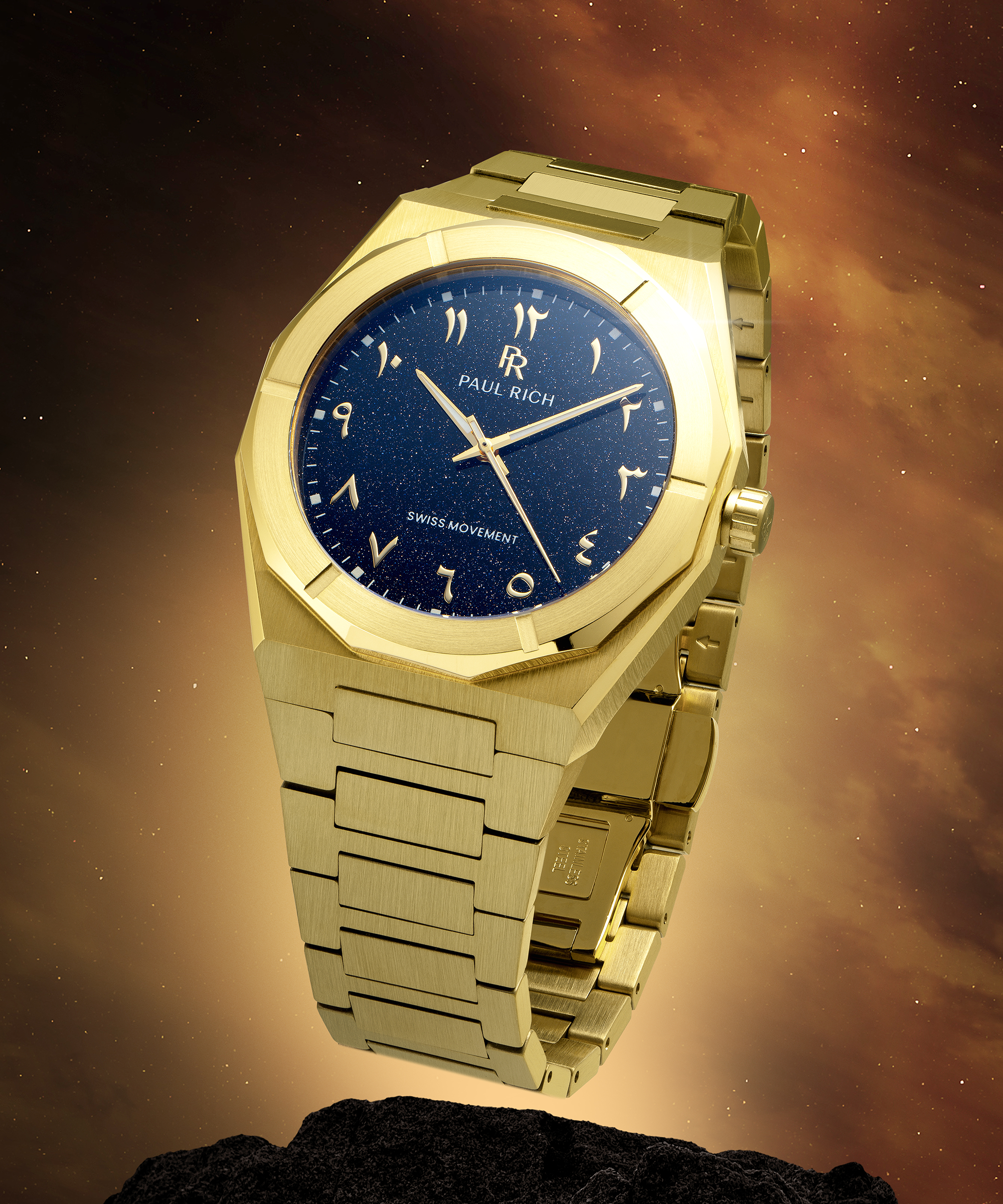 Gold Paul Rich watch with blue aventurine dial and Arabic numerals, shown on a rock with glowing space-themed background.