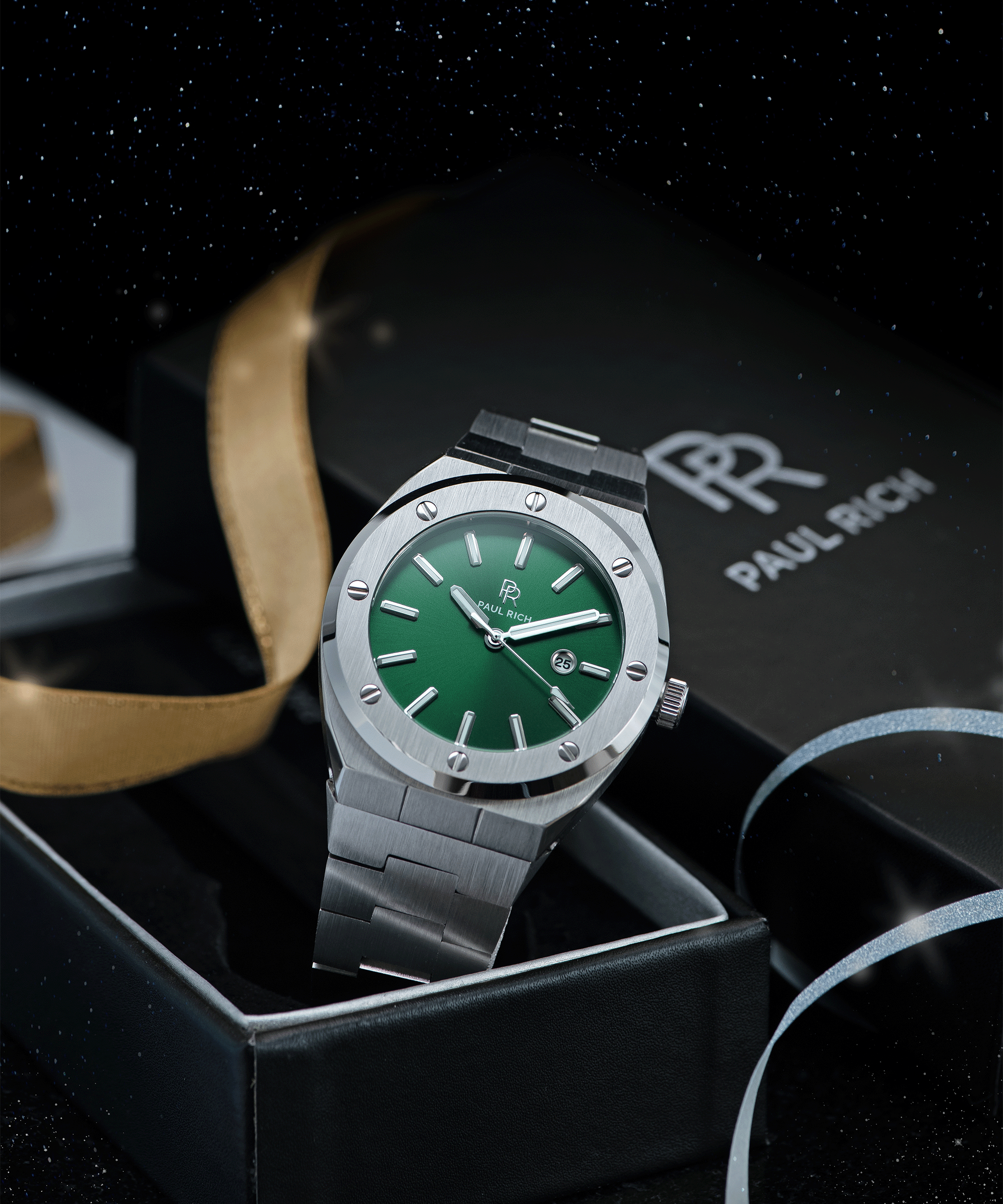 Paul Rich brushed silver watch with green dial and date window, displayed in open gift box with gold ribbon and starry night background.