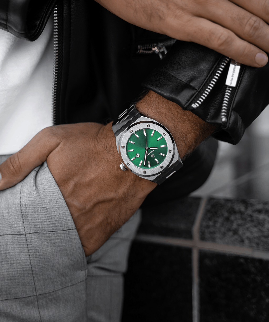 Paul Rich brushed silver watch with green dial and date window, worn with black leather jacket and gray plaid pants, hand in pocket.