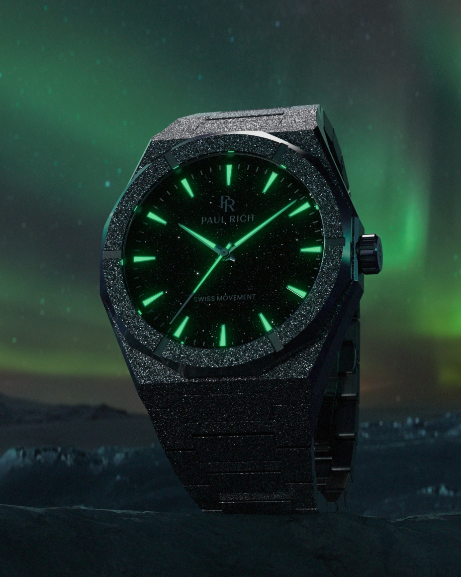 Black frosted Paul Rich watch with glowing green markers and hands, set against an aurora-lit night sky and icy mountain landscape.