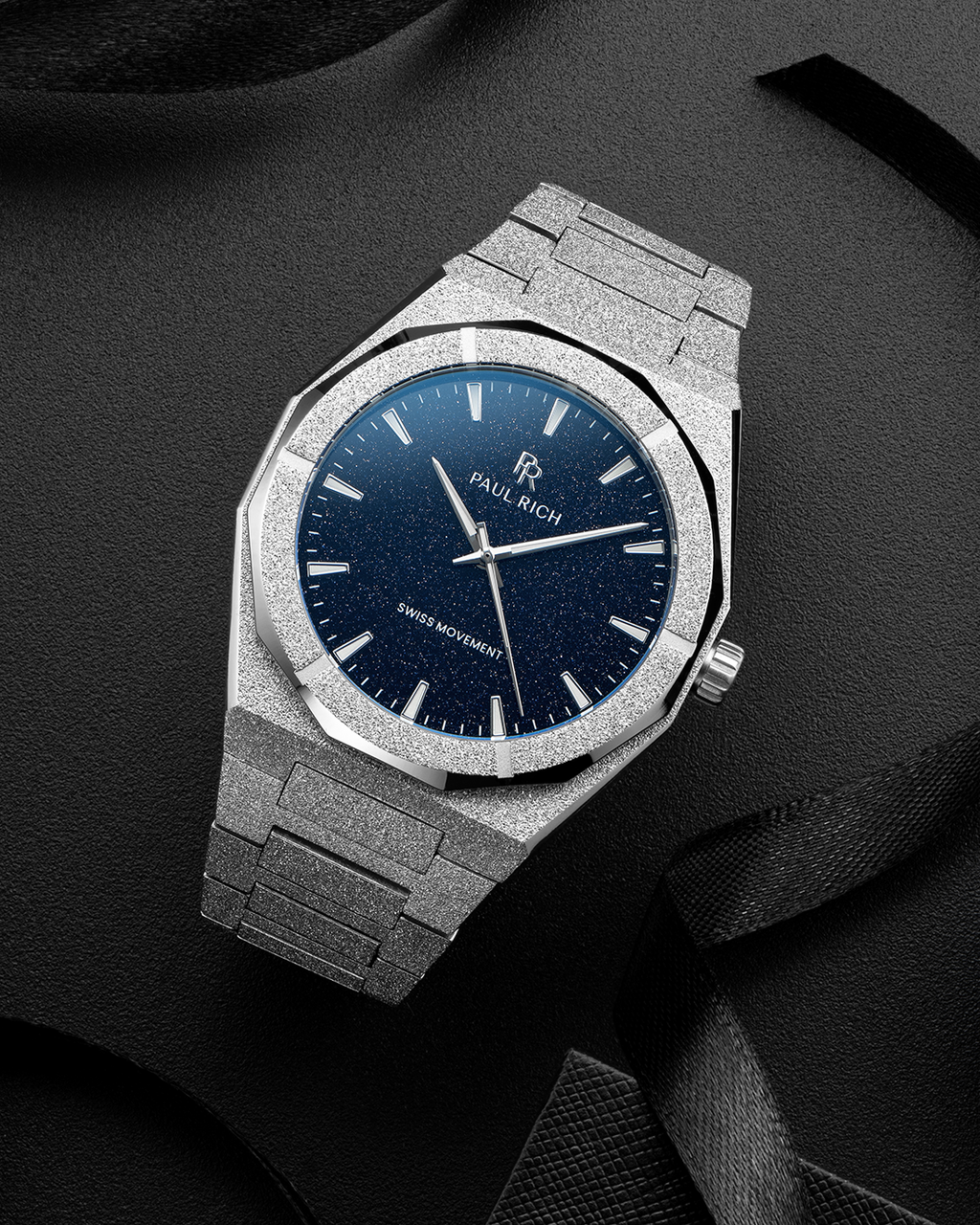 Silver frosted Paul Rich watch with a blue aventurine dial, displayed on textured black surface with black ribbon accents.