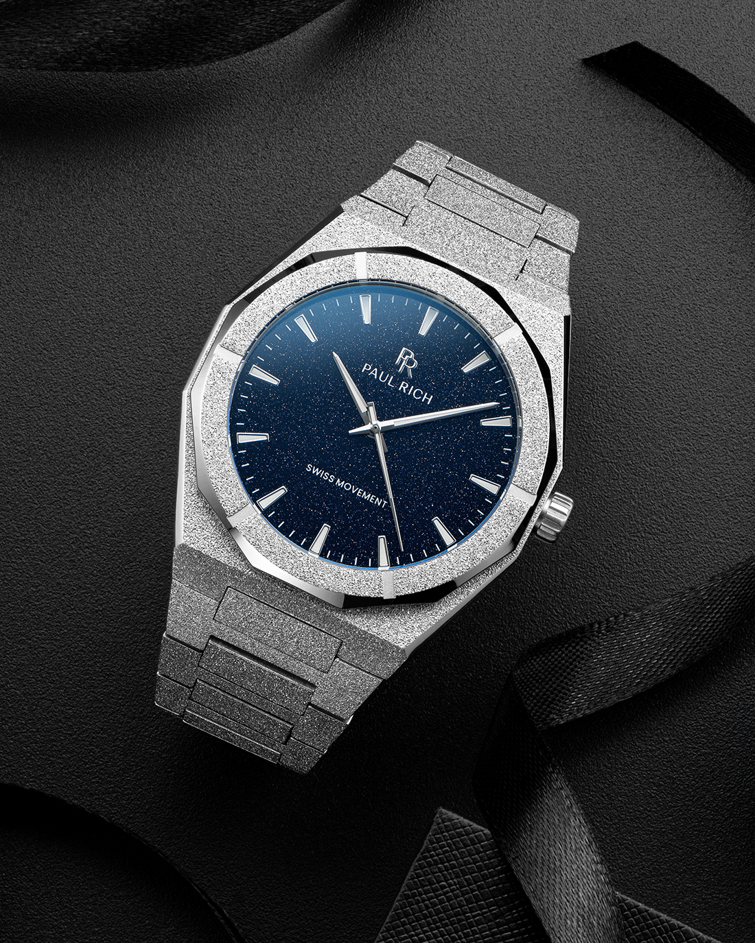 Silver frosted Paul Rich watch with a blue aventurine dial, displayed on textured black surface with black ribbon accents.