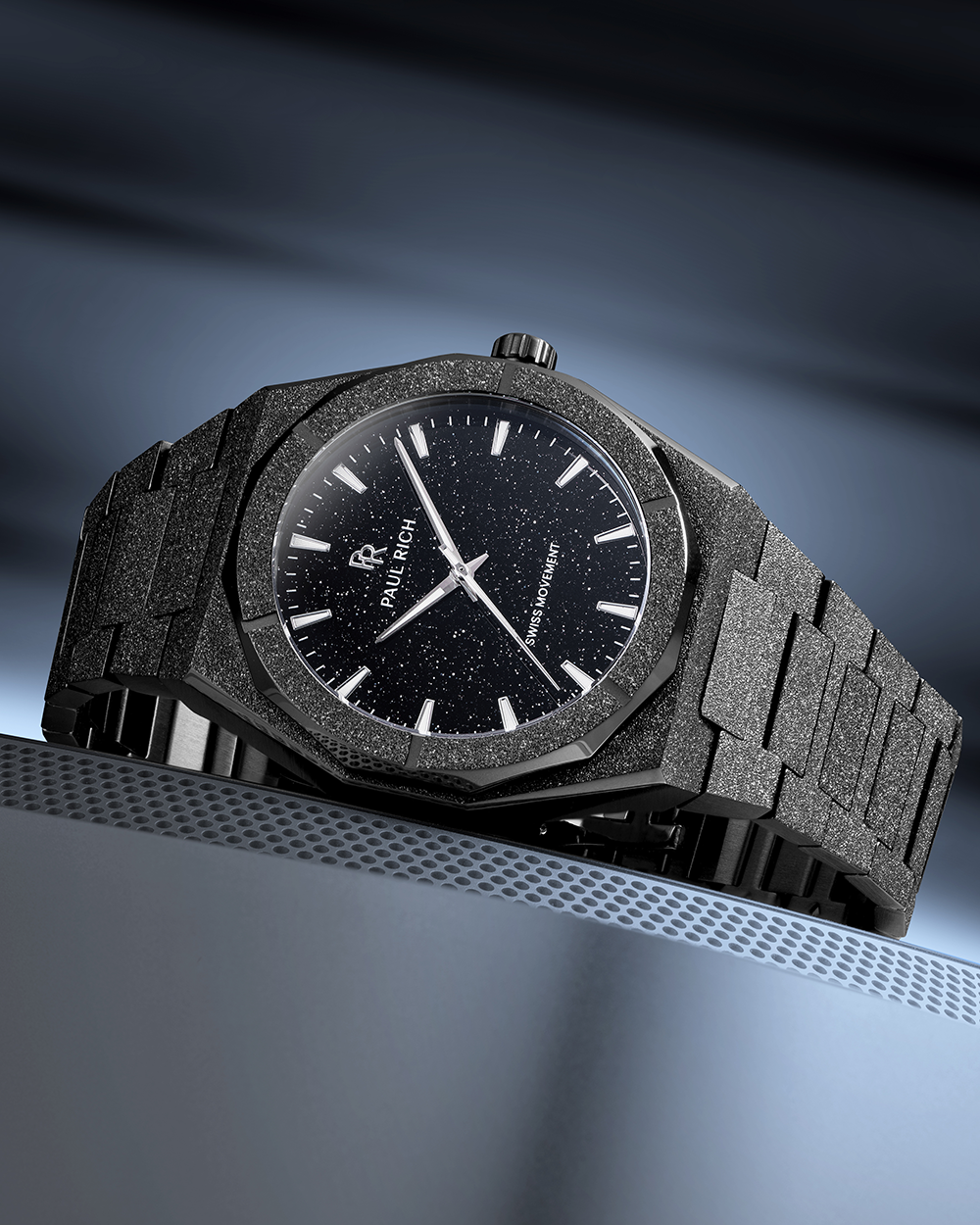 Paul Rich watch with frosted black case and black aventurine dial, displayed on a sleek metallic surface with cool blue lighting.