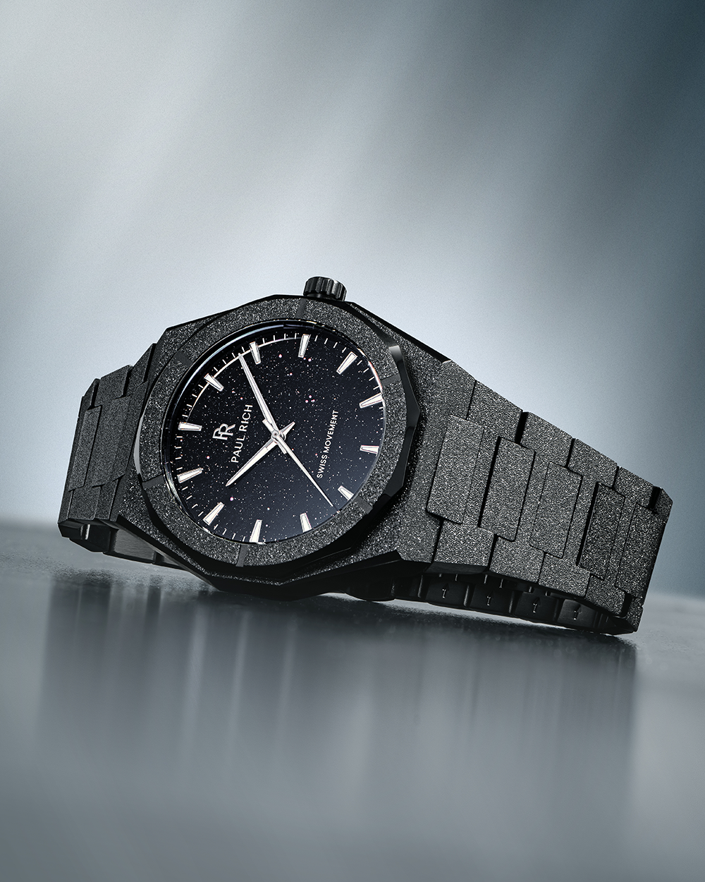 Paul Rich watch with frosted black case and black aventurine dial, resting on a reflective surface with soft gradient lighting.