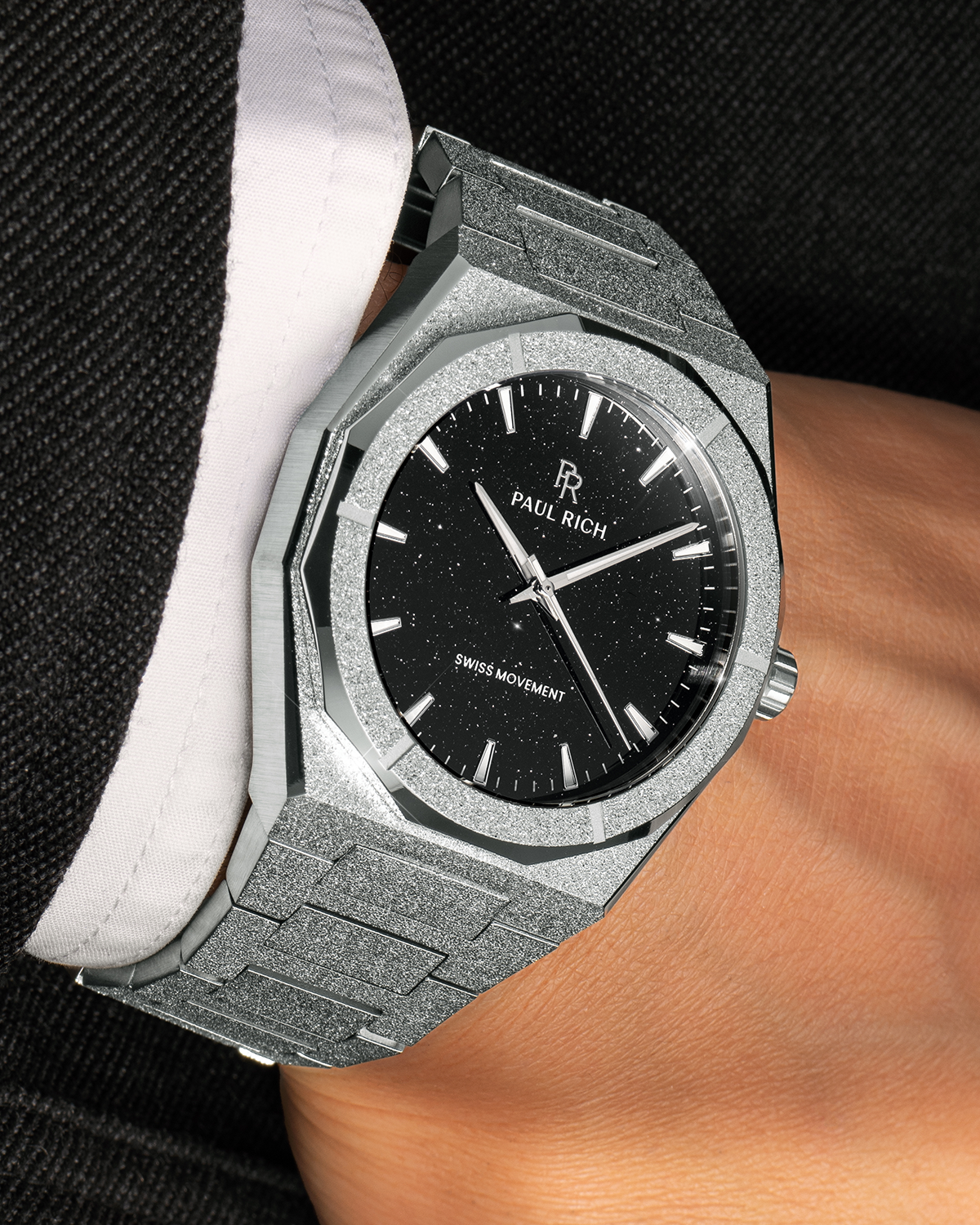 Paul Rich watch with frosted silver case and black aventurine dial, worn on wrist with a black textured suit and white cuff.